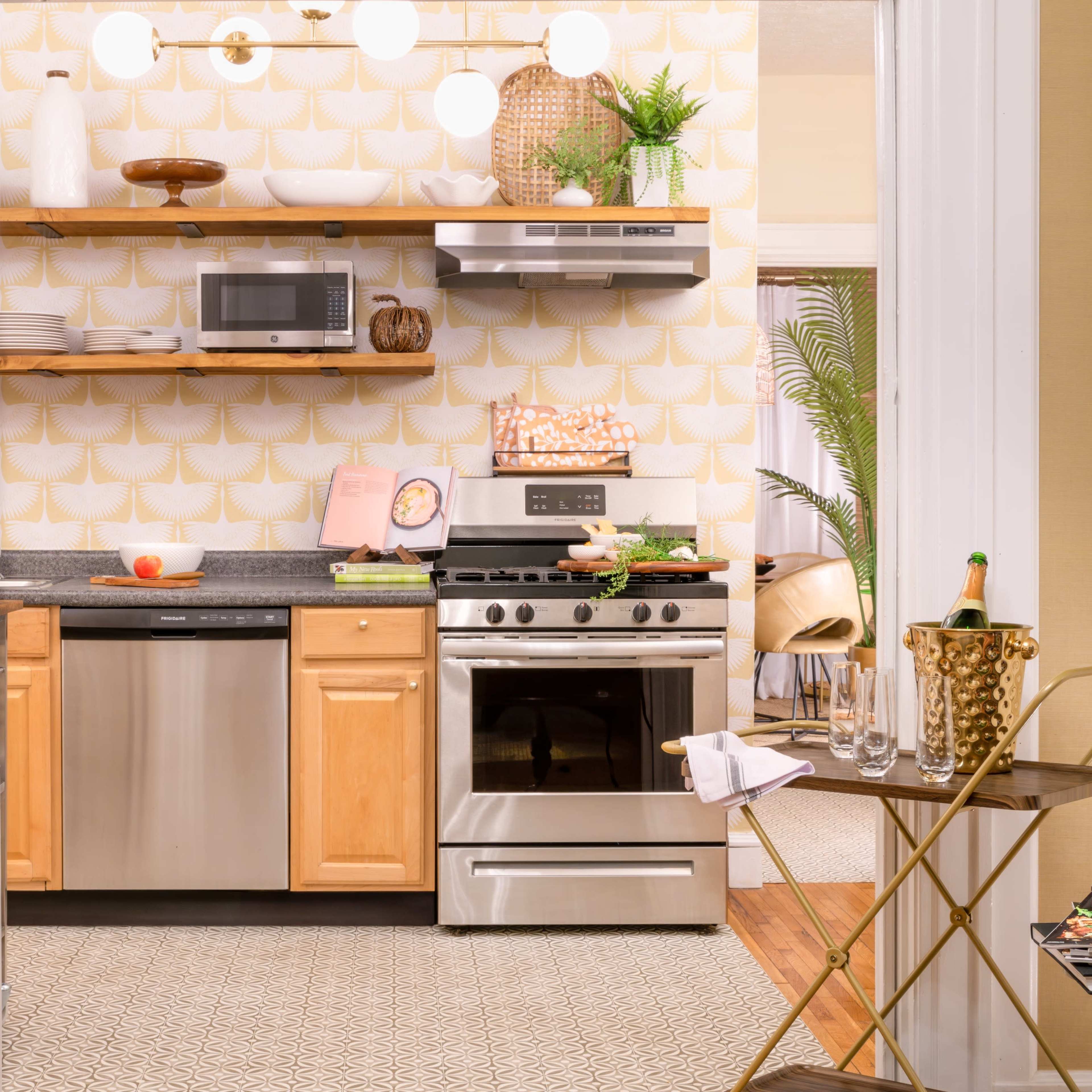 A modern kitchen features stainless steel appliances, wooden cabinetry, and decorative shelving against a patterned wallpaper.