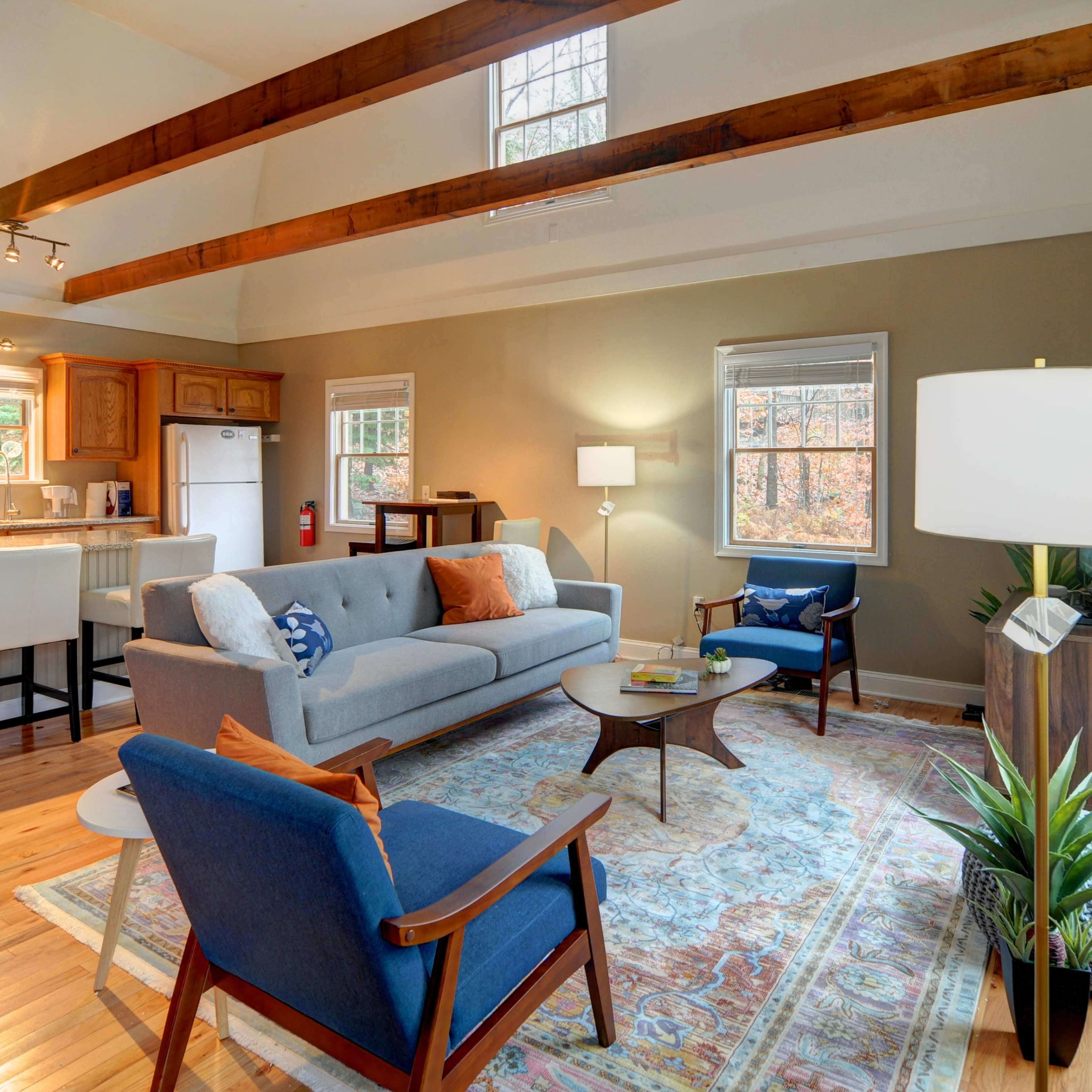 A bright living room with a gray sofa, wooden beams on the ceiling, and a cozy seating arrangement featuring a blue chair and a round coffee table.