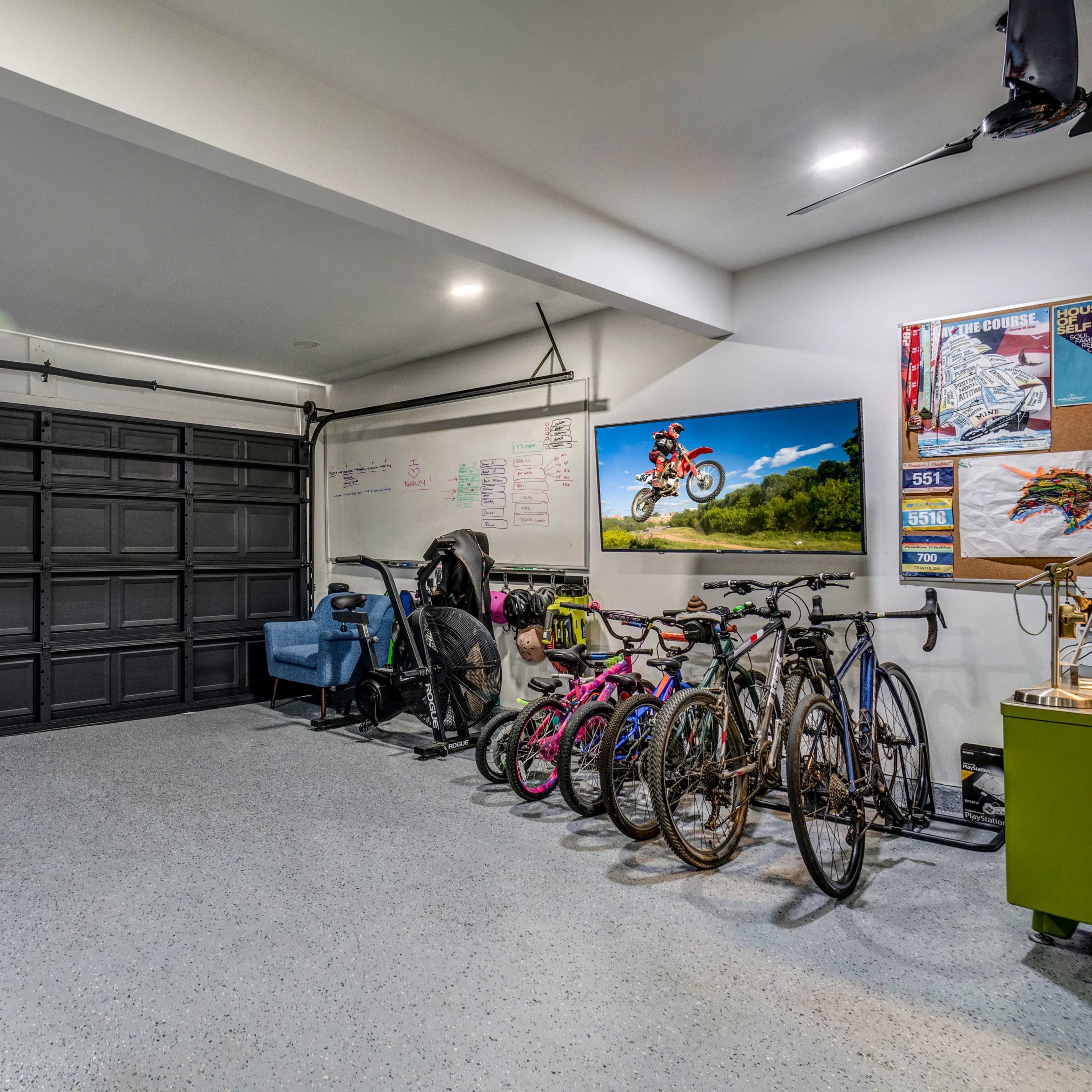 A spacious garage with a closed black garage door, several bicycles lined up against the wall, and storage items organized on shelves and a bulletin board.
