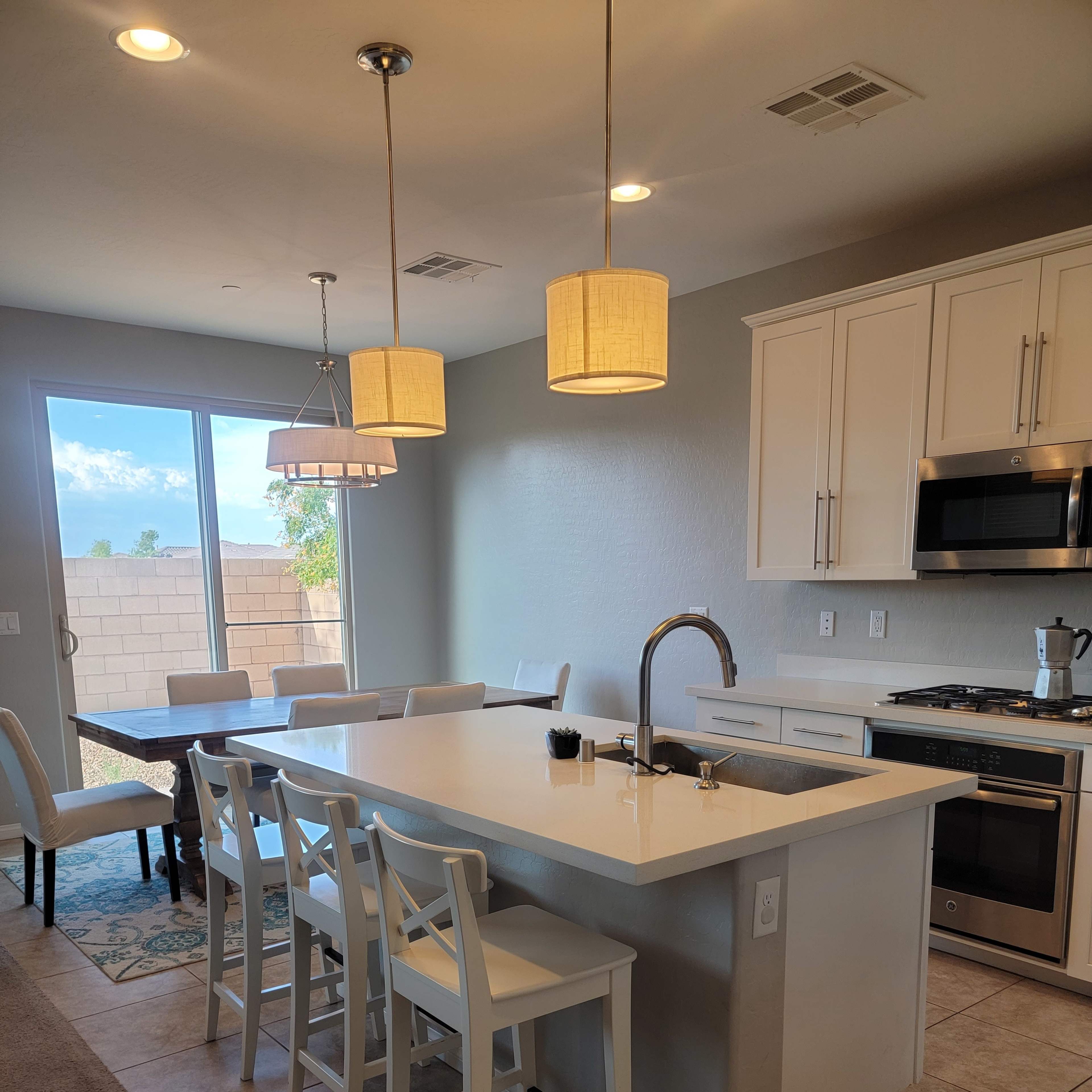A modern kitchen features a large island with bar stools, a dining table, and sliding glass doors leading to an outdoor area.