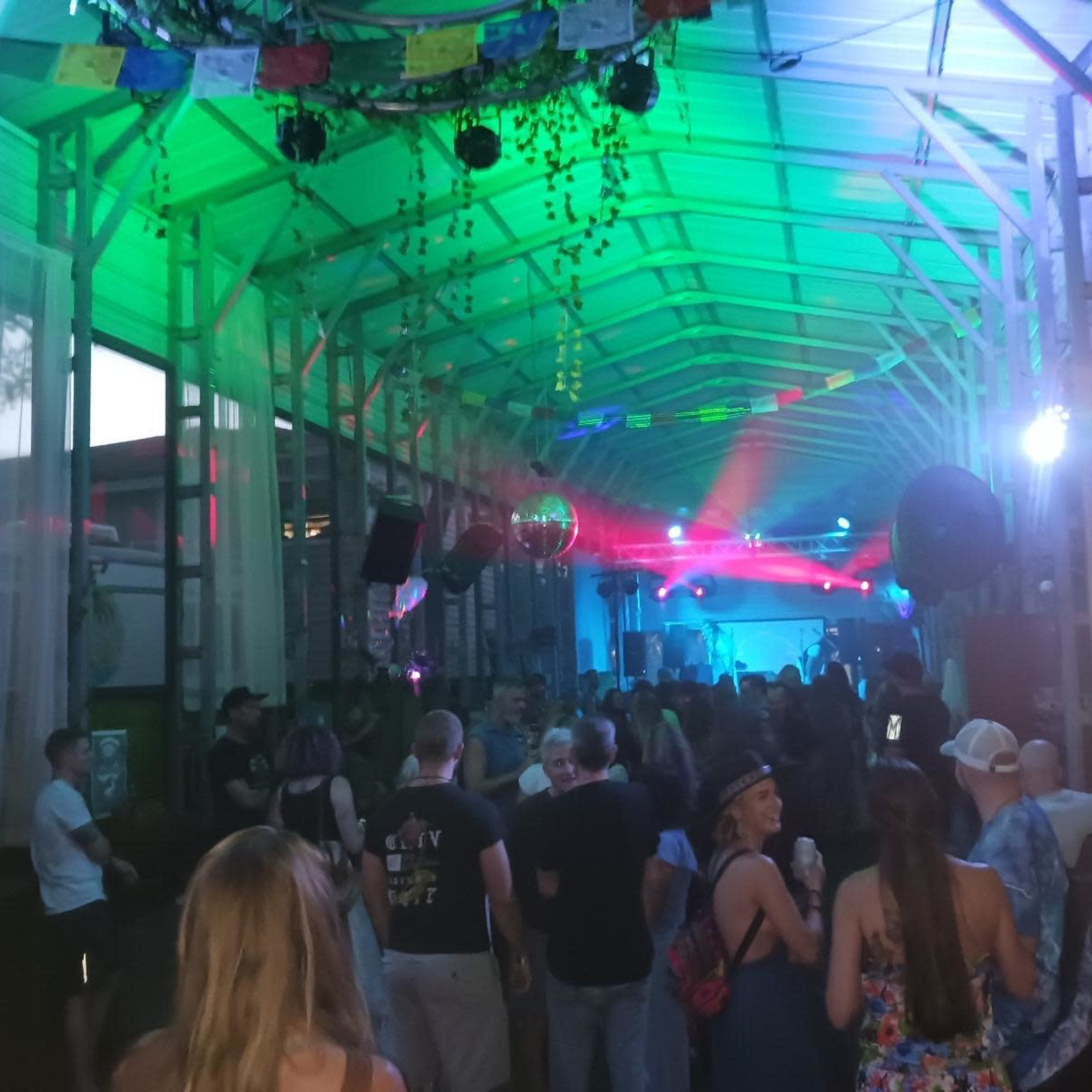 A crowded indoor space with colorful lights and a stage at one end, filled with people enjoying a live music performance.