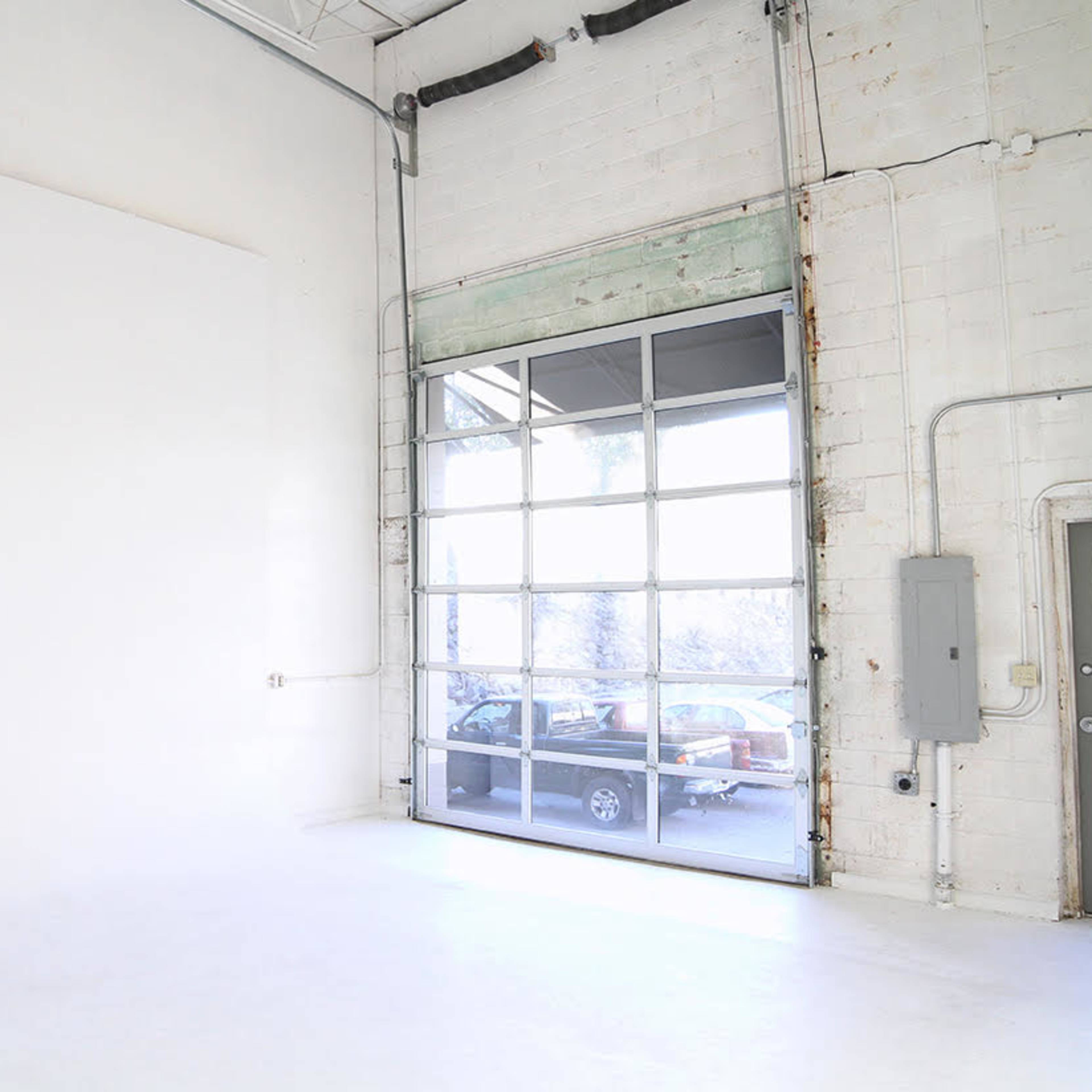 A spacious, empty studio with a large glass garage door and a smooth white floor.