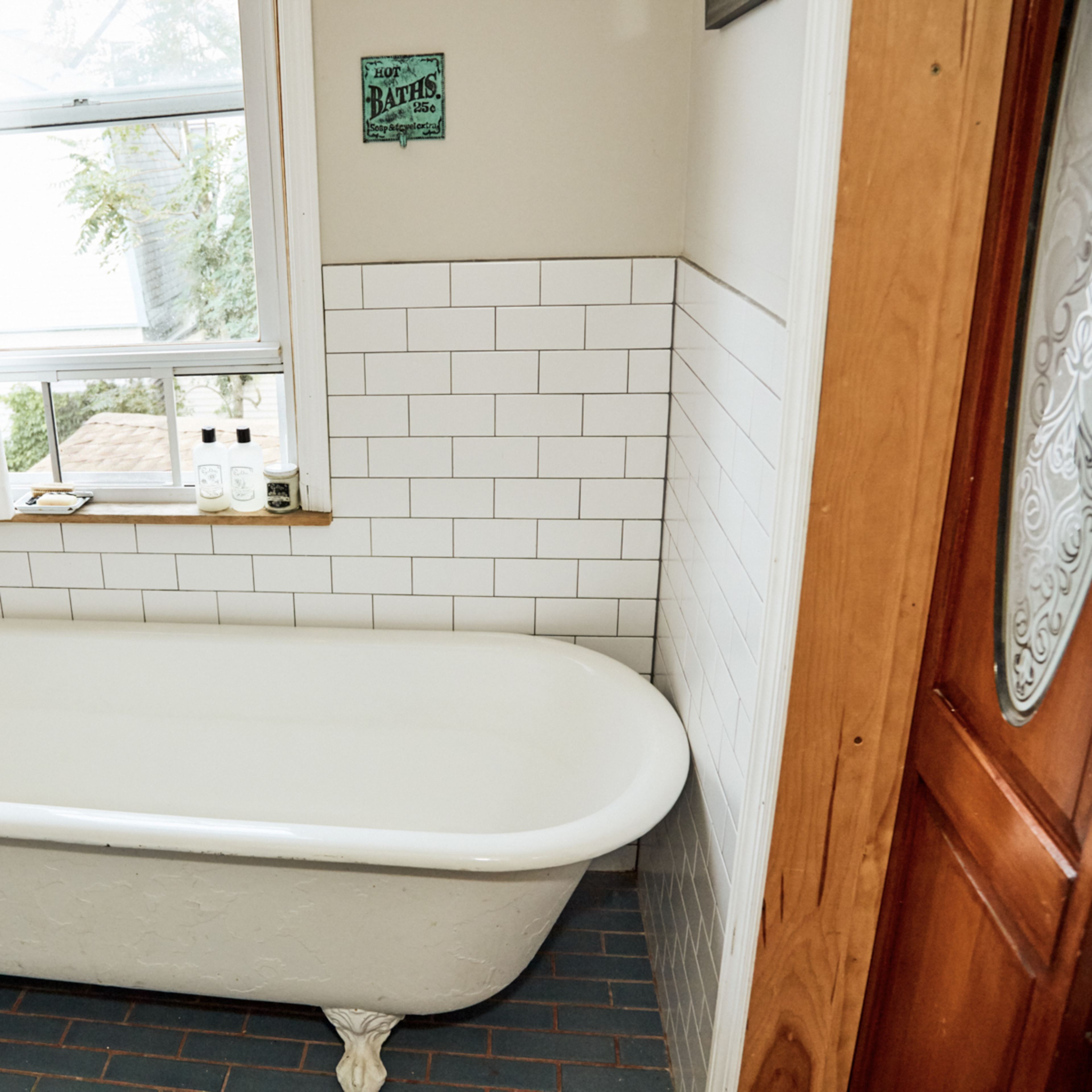 A vintage-style bathtub with claw feet positioned near a window, accompanied by a wooden ladder and tiled floor.