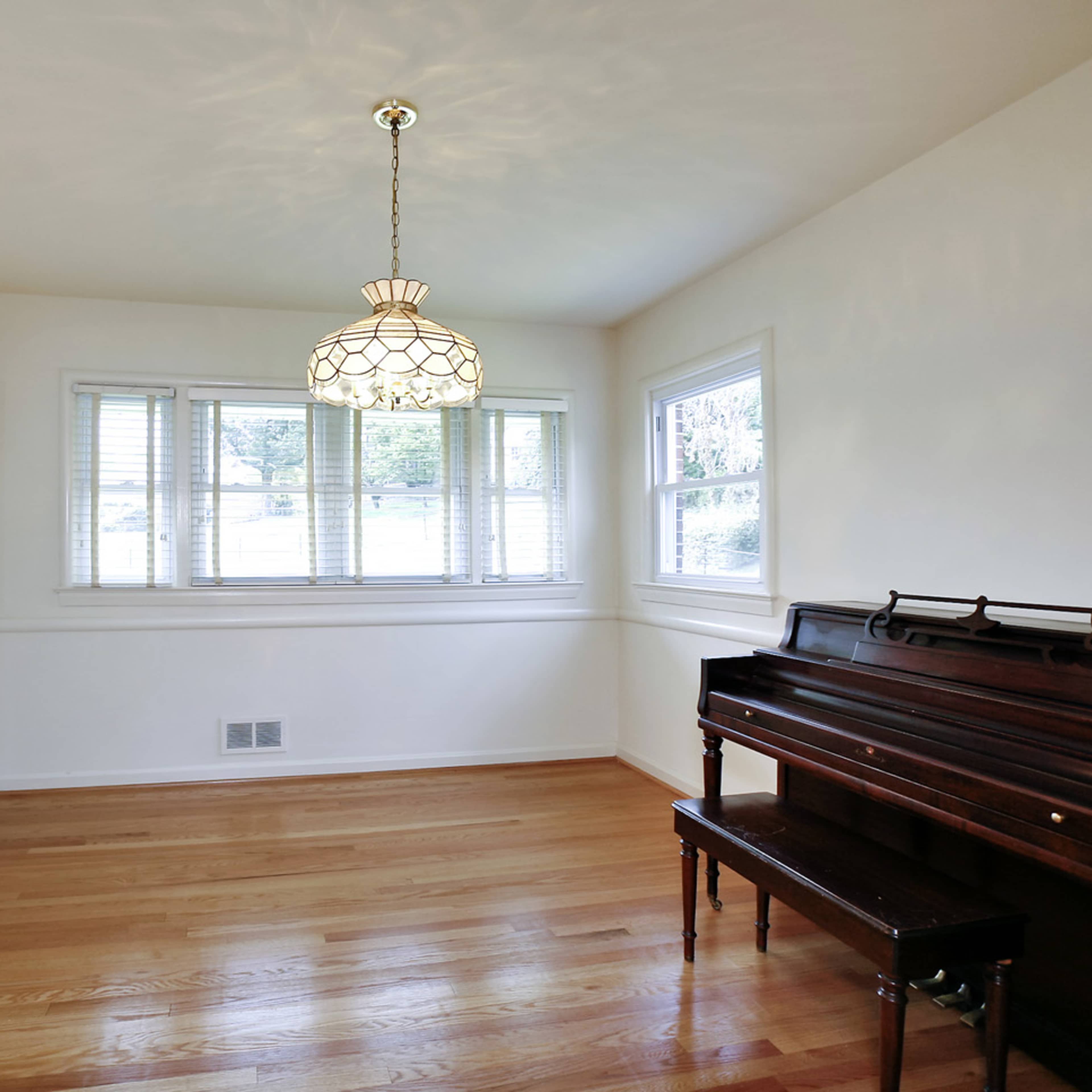 A room featuring a piano, a light fixture, and large windows that provide natural light.