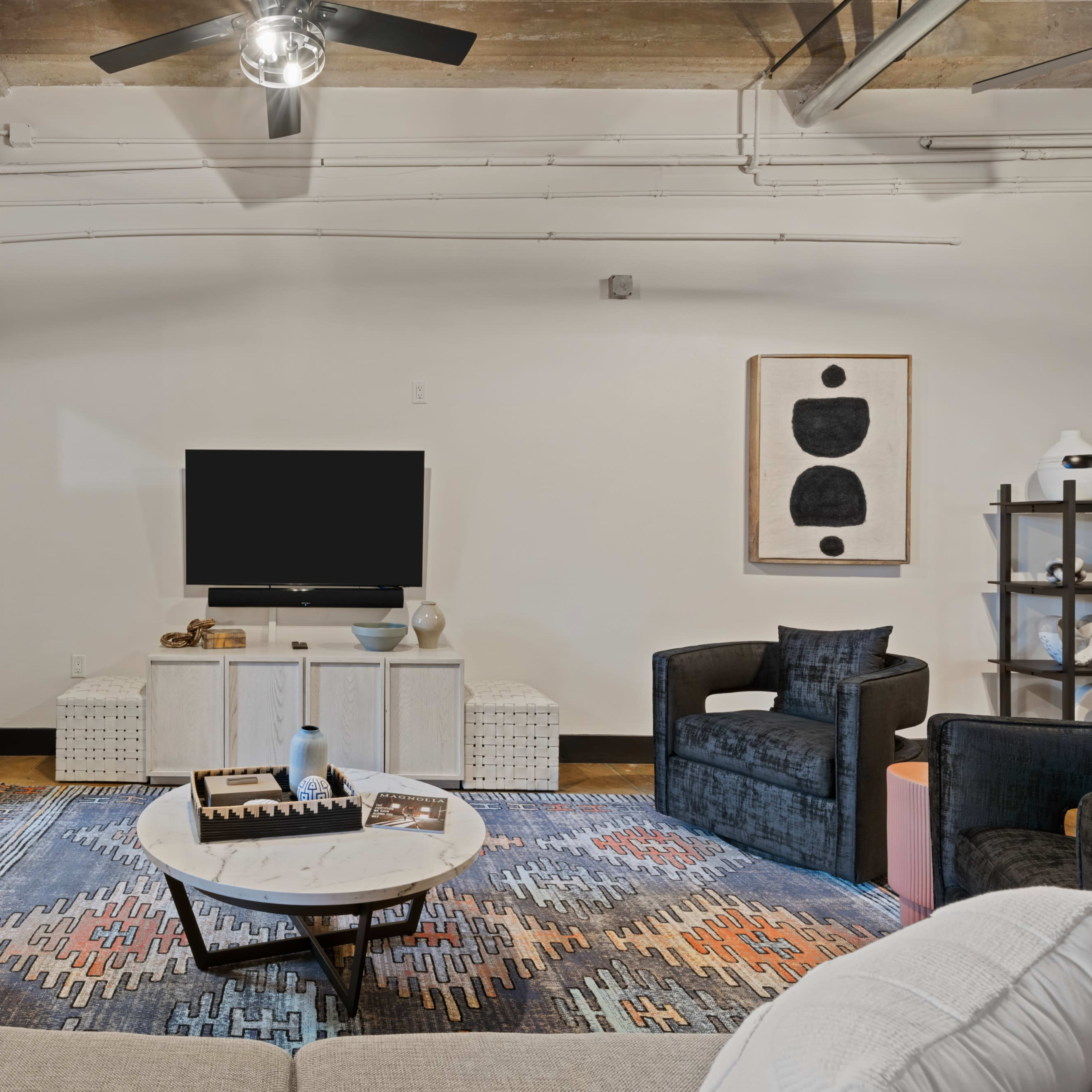 A modern living room with a flat-screen TV mounted on the wall, a neutral-colored sofa, a round coffee table, and two armchairs situated around a patterned area rug.