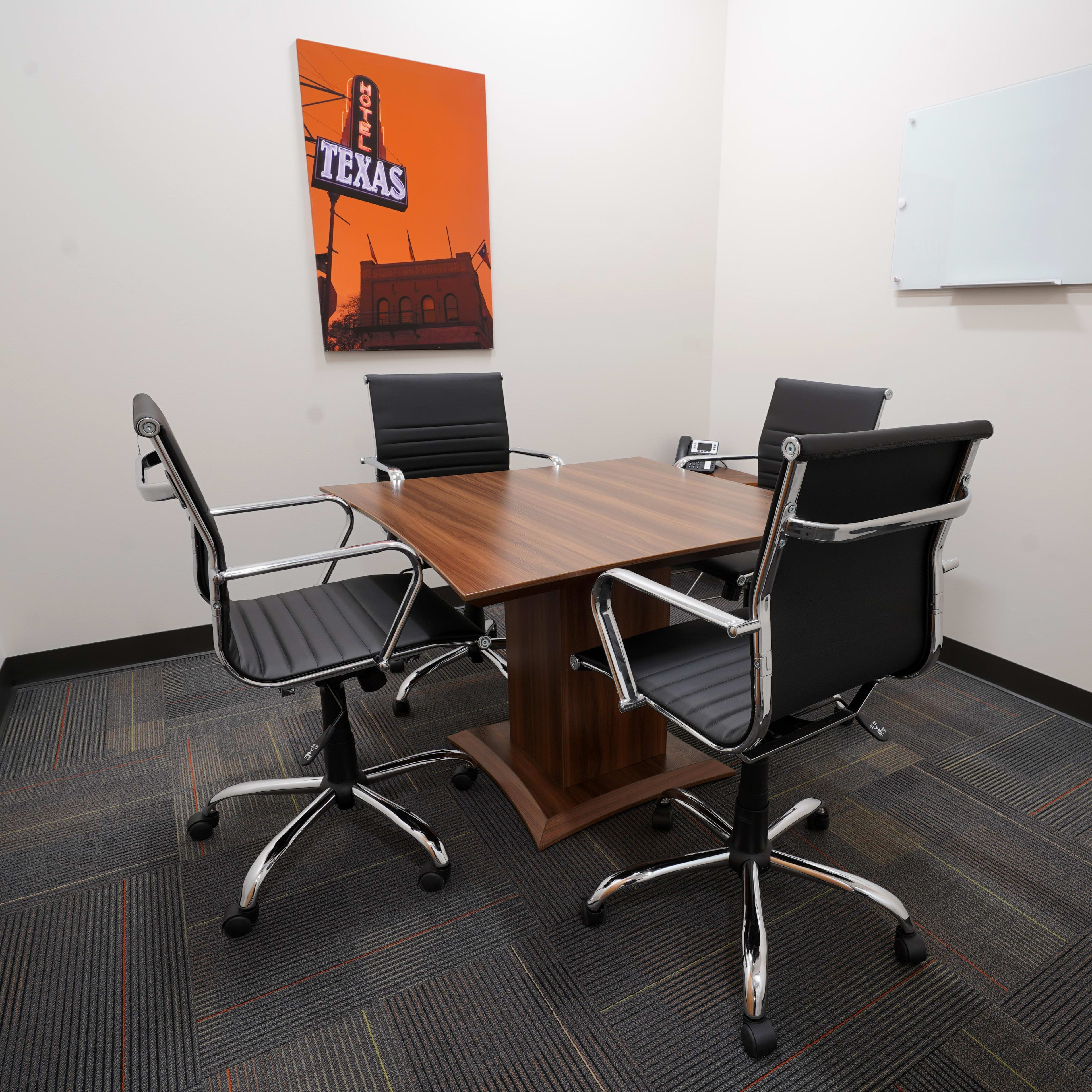 A small conference room features a wooden table surrounded by three black office chairs and a Texas-themed artwork on the wall.