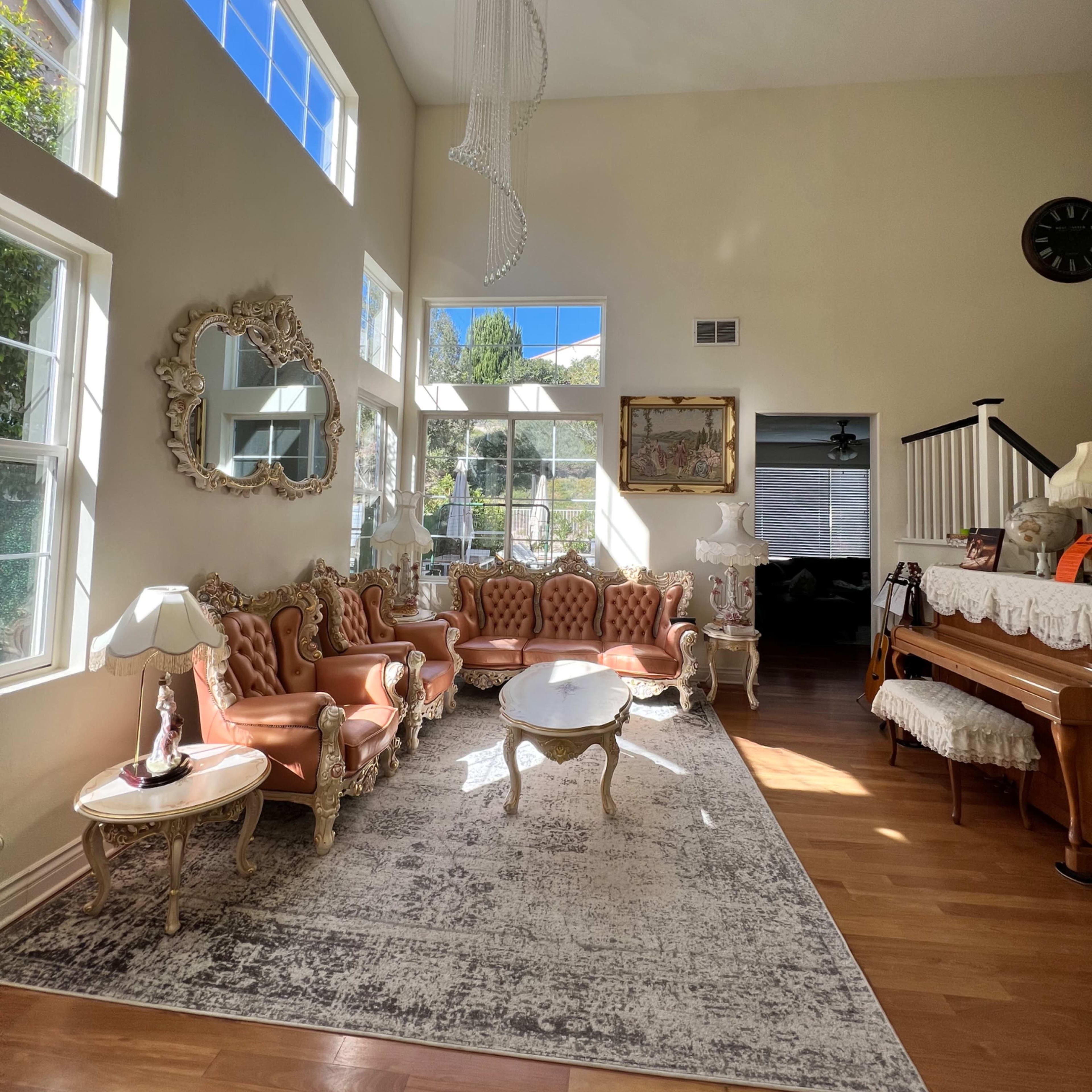 A spacious living room with large windows, featuring a set of pink tufted sofas, a round coffee table, a piano, and decorative art on the walls.