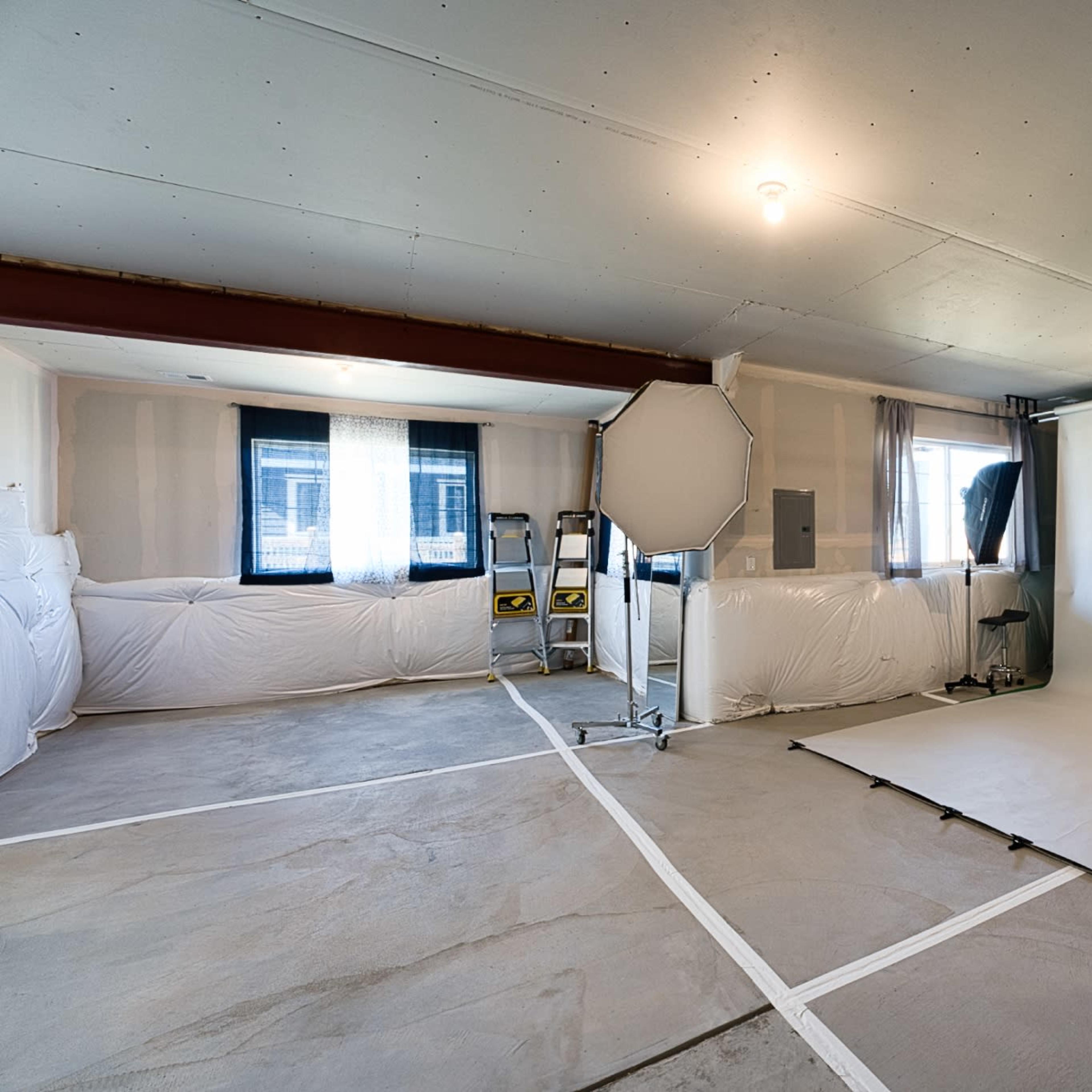 A photography studio with a spacious setup featuring a white backdrop, softbox lighting, and a ladder against the wall.