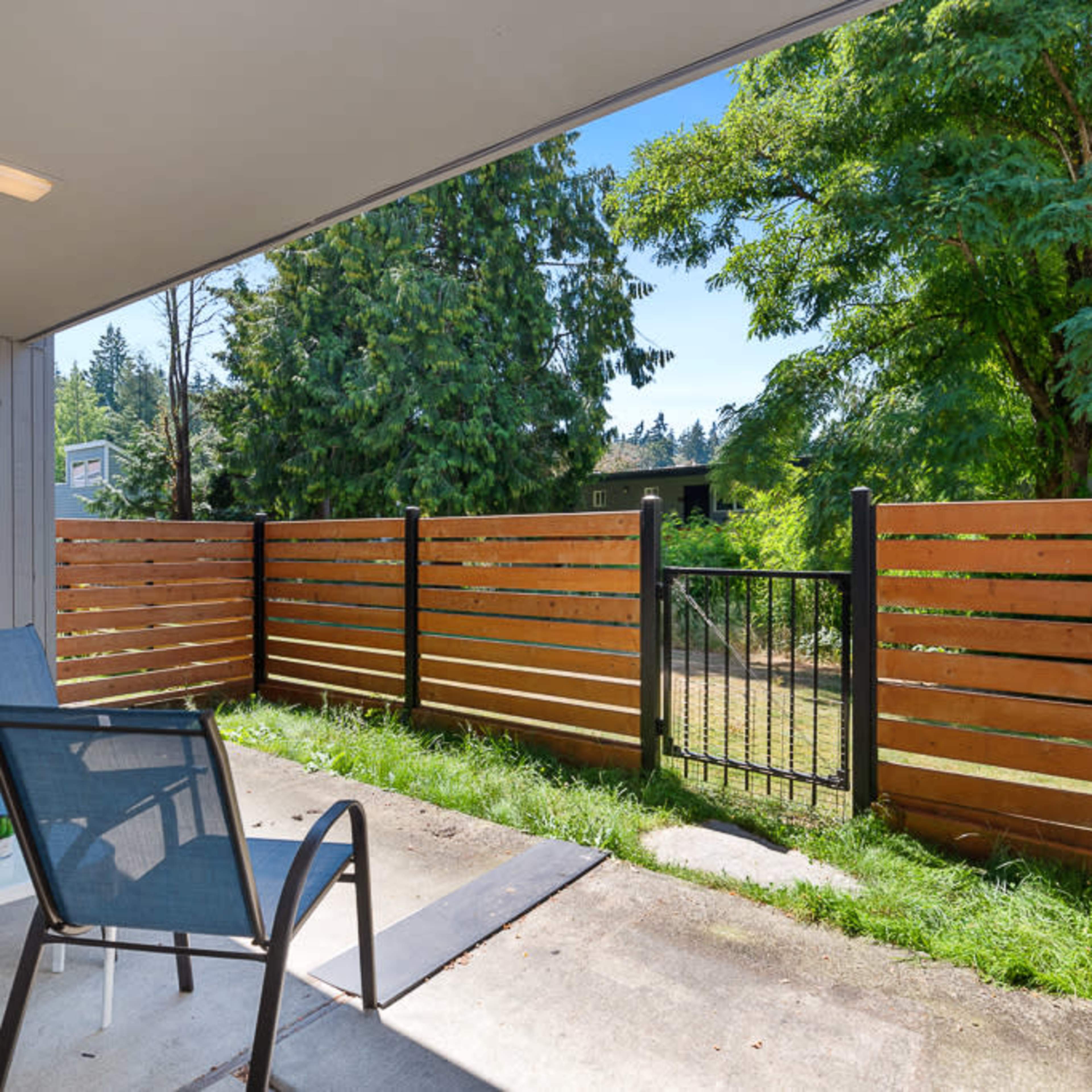 A patio area with two chairs and a small table overlooking a fenced yard and trees.