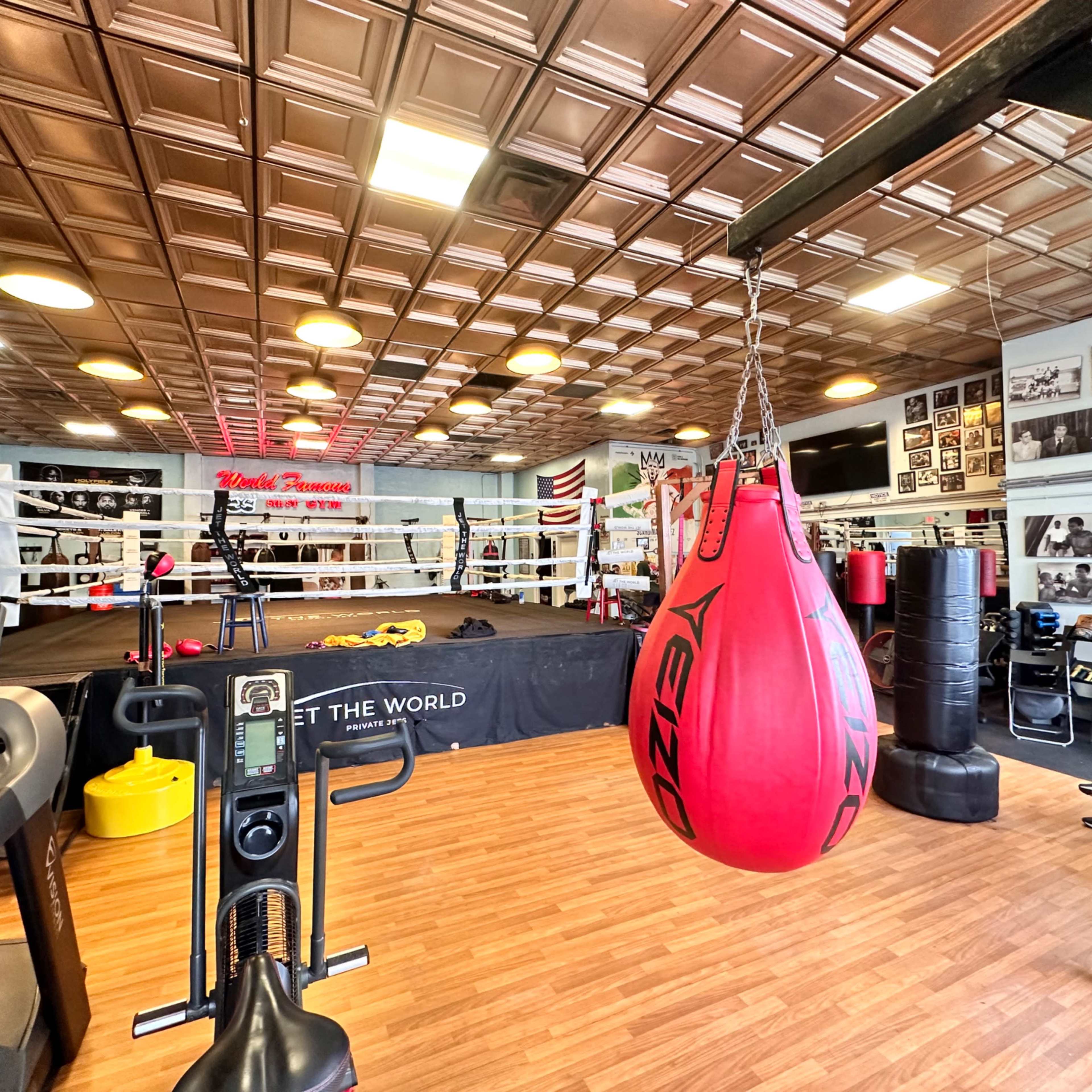 A boxing gym featuring a ring, exercise equipment, and colorful wall decorations, including photographs and a sign.