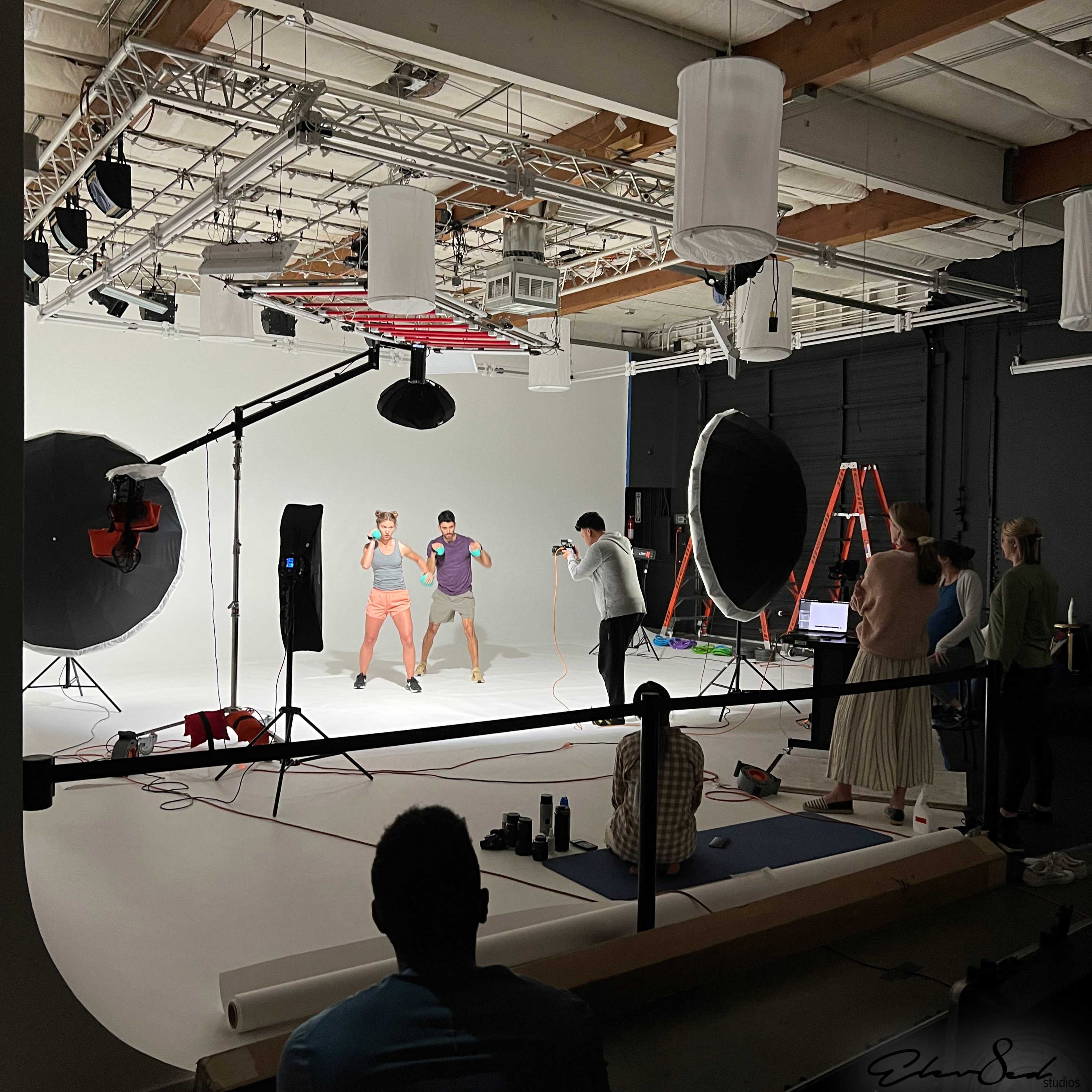 A photography studio features a group of people engaged in a photoshoot with various lighting equipment and backdrops set up.