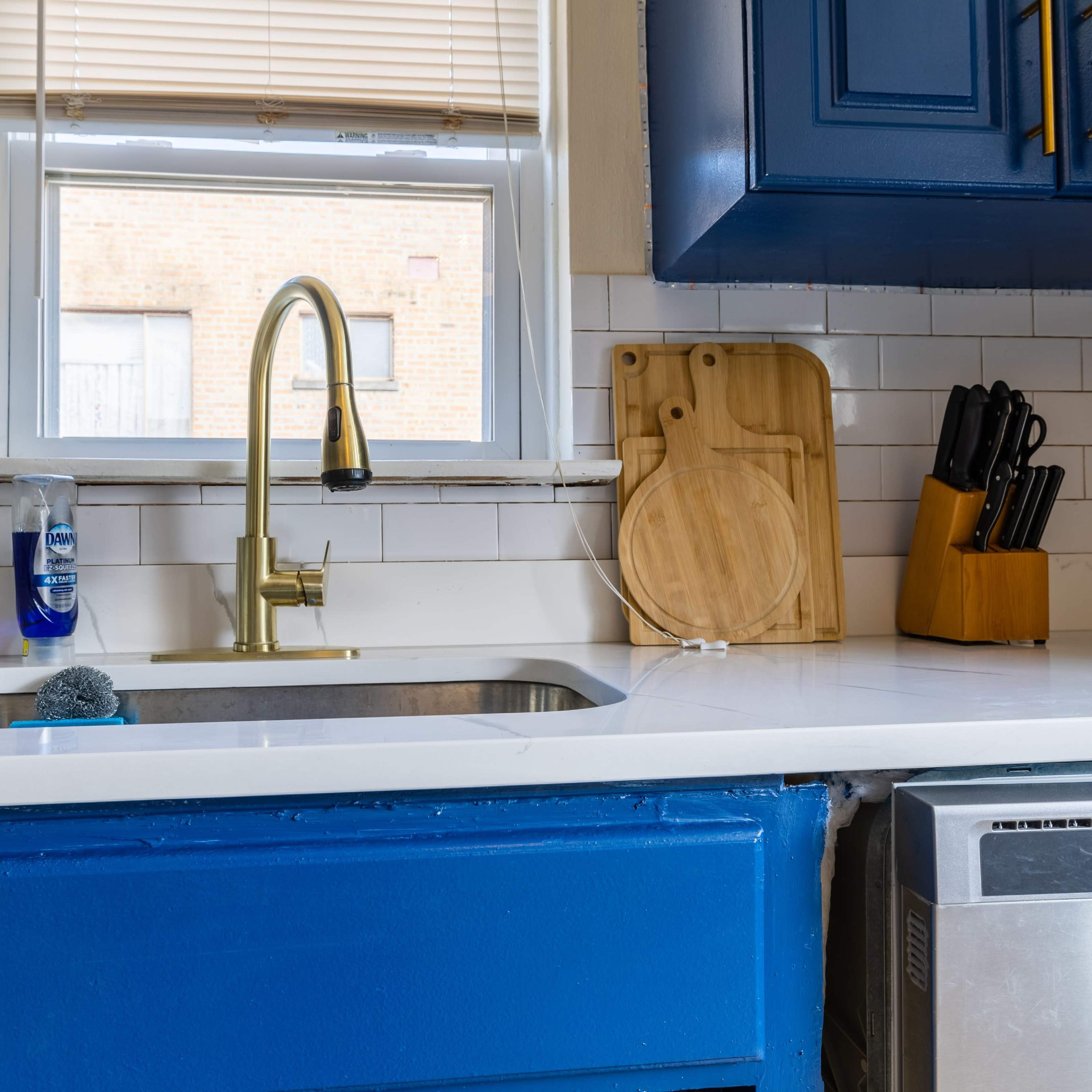 A blue kitchen with a sink, a wooden cutting board, and a knife block on a countertop.