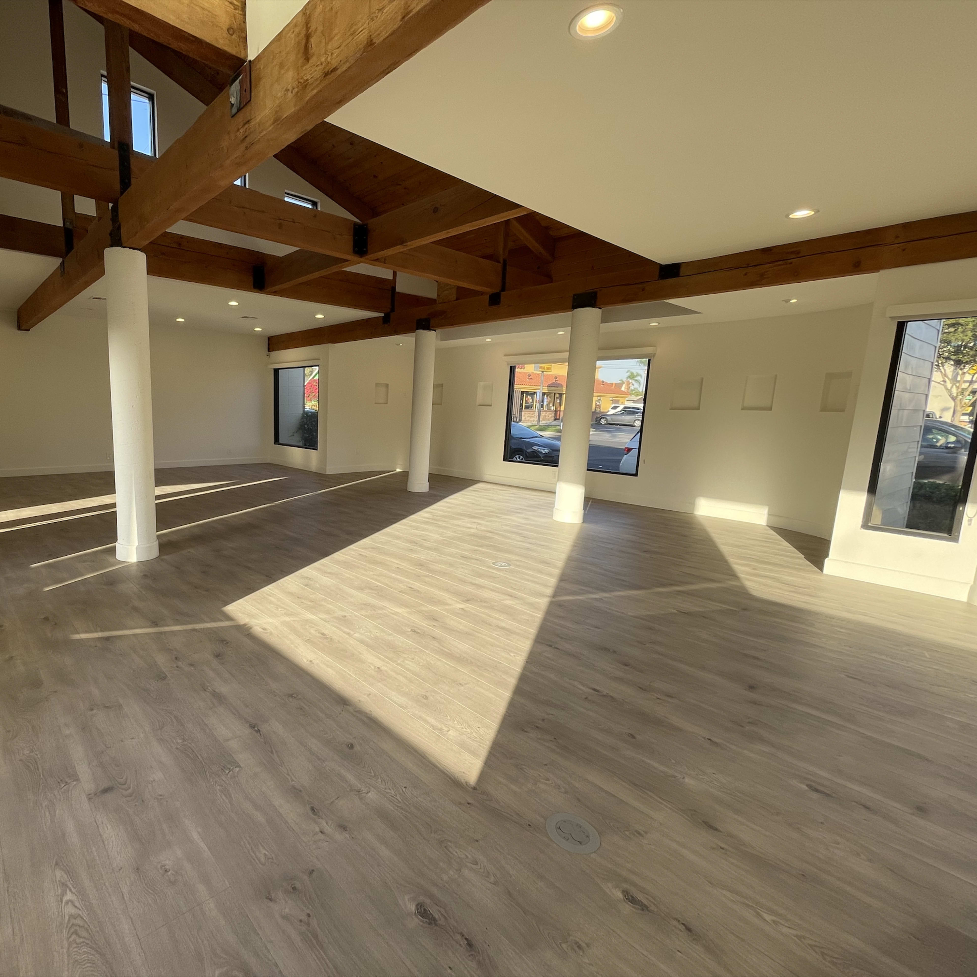 An empty room with wooden beams, large windows, and laminate flooring.