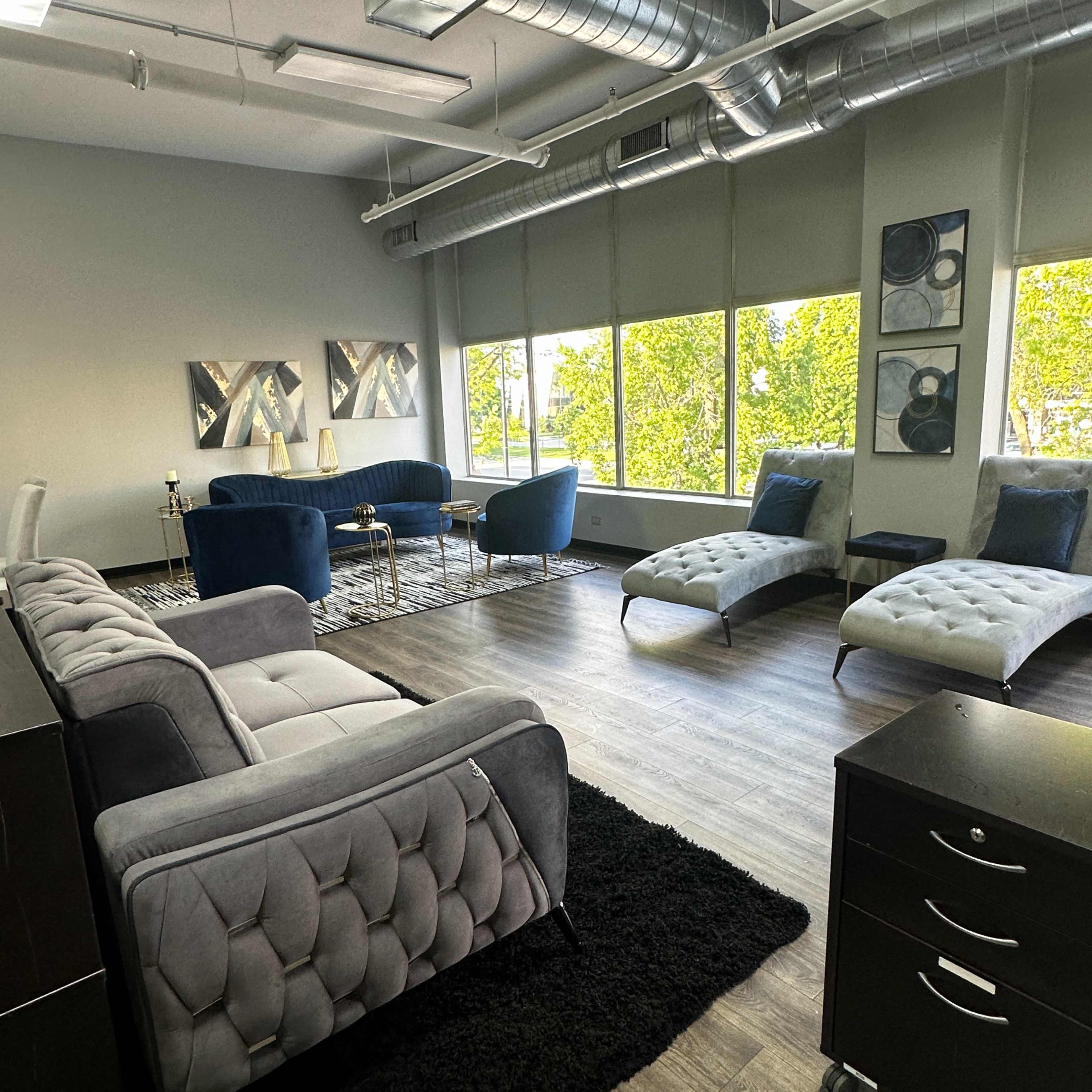 A modern office space features gray and blue furniture with large windows that allow natural light to illuminate the room.