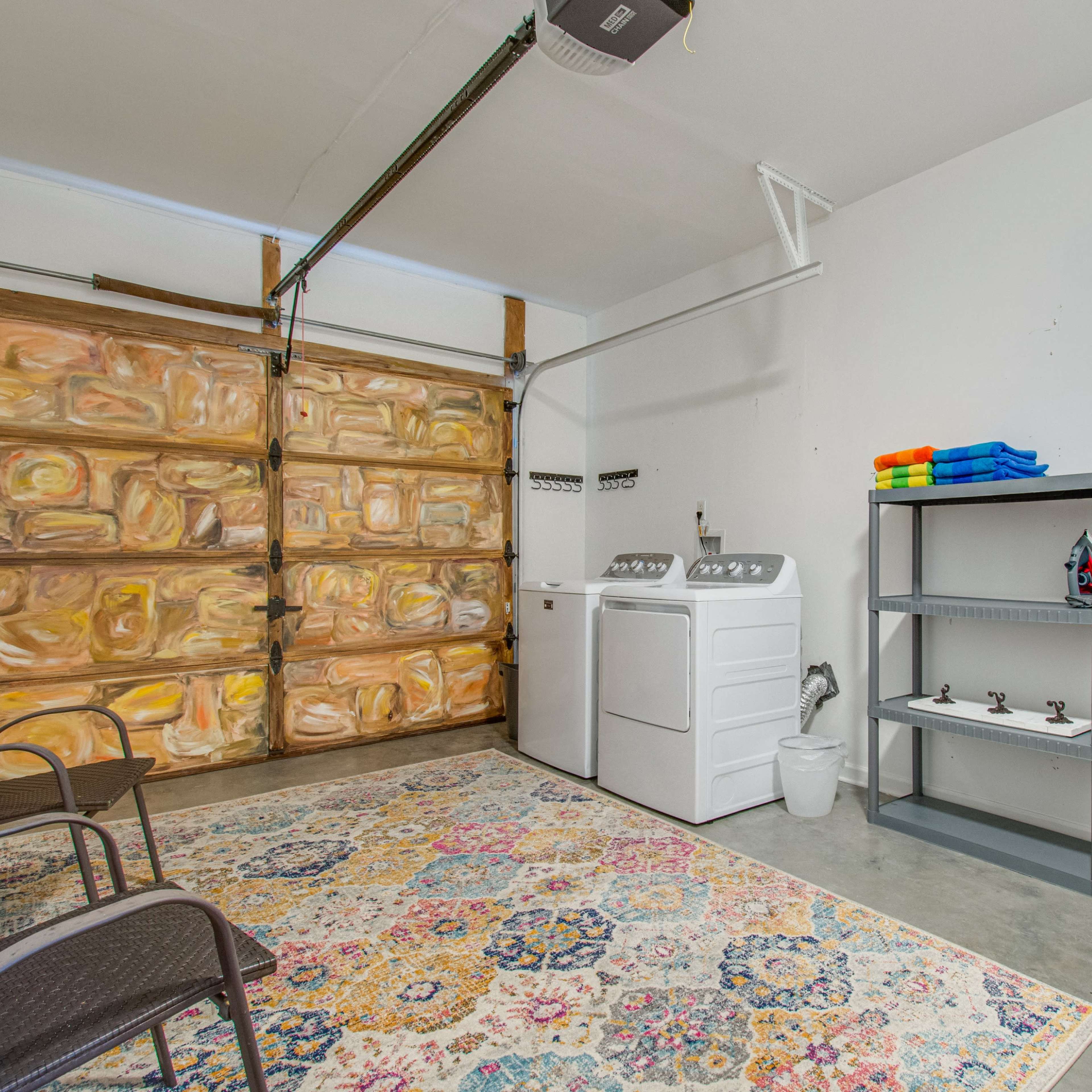 A garage featuring a washing machine and dryer, a patterned rug on the floor, a shelving unit, an ironing board, and a wooden garage door.