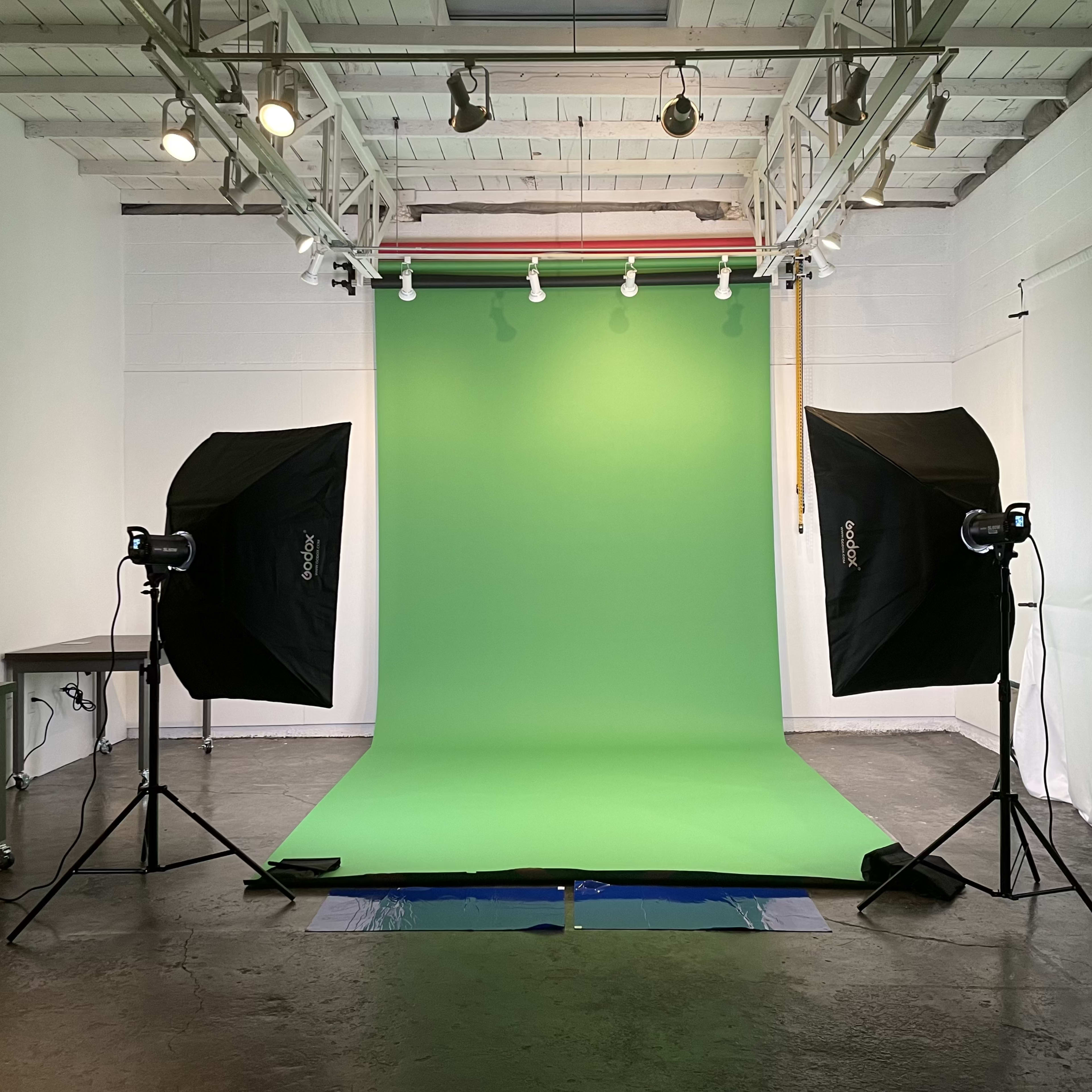 A photography studio with a green backdrop and two softbox lights positioned on either side.