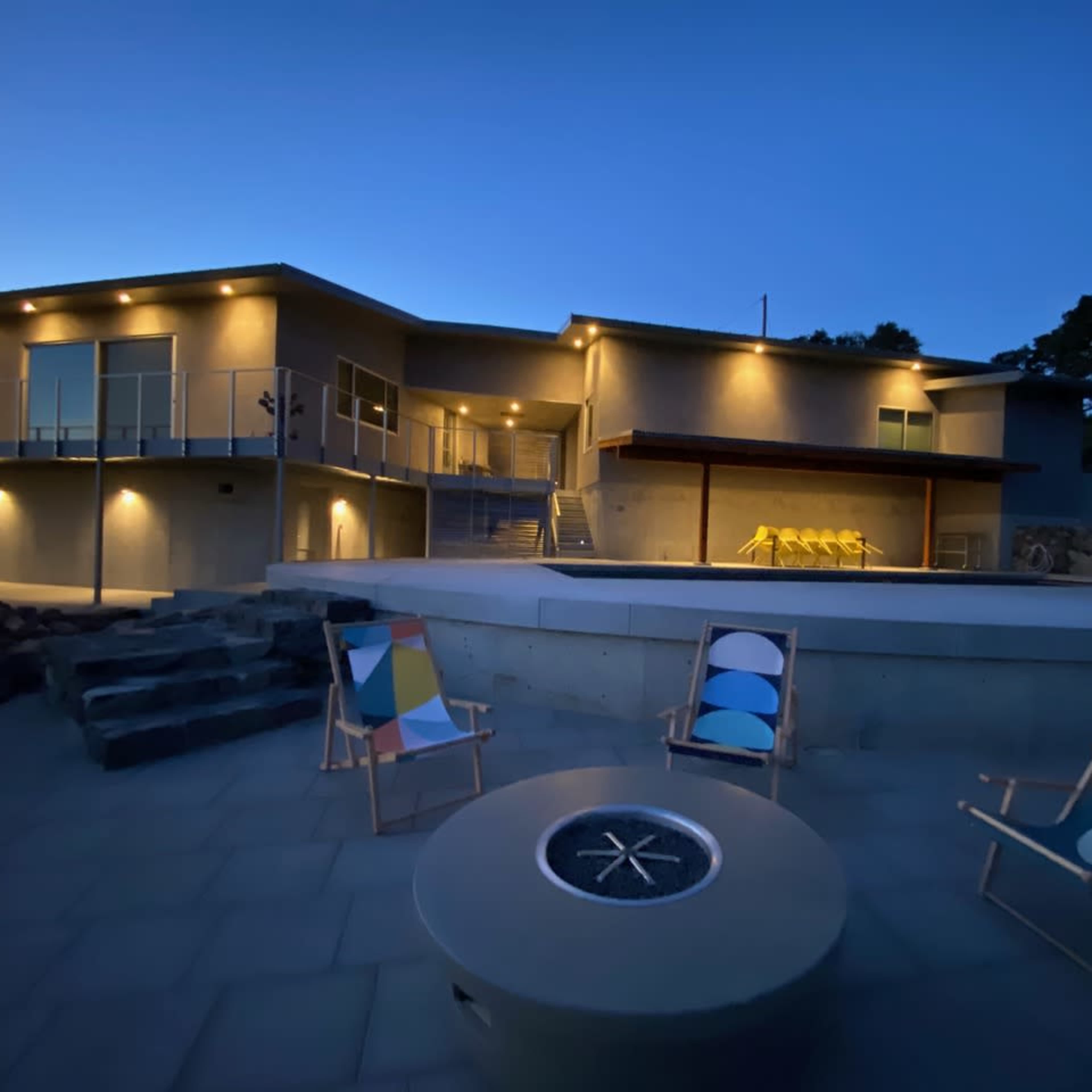 A modern house with outdoor seating and a pool is illuminated at dusk.