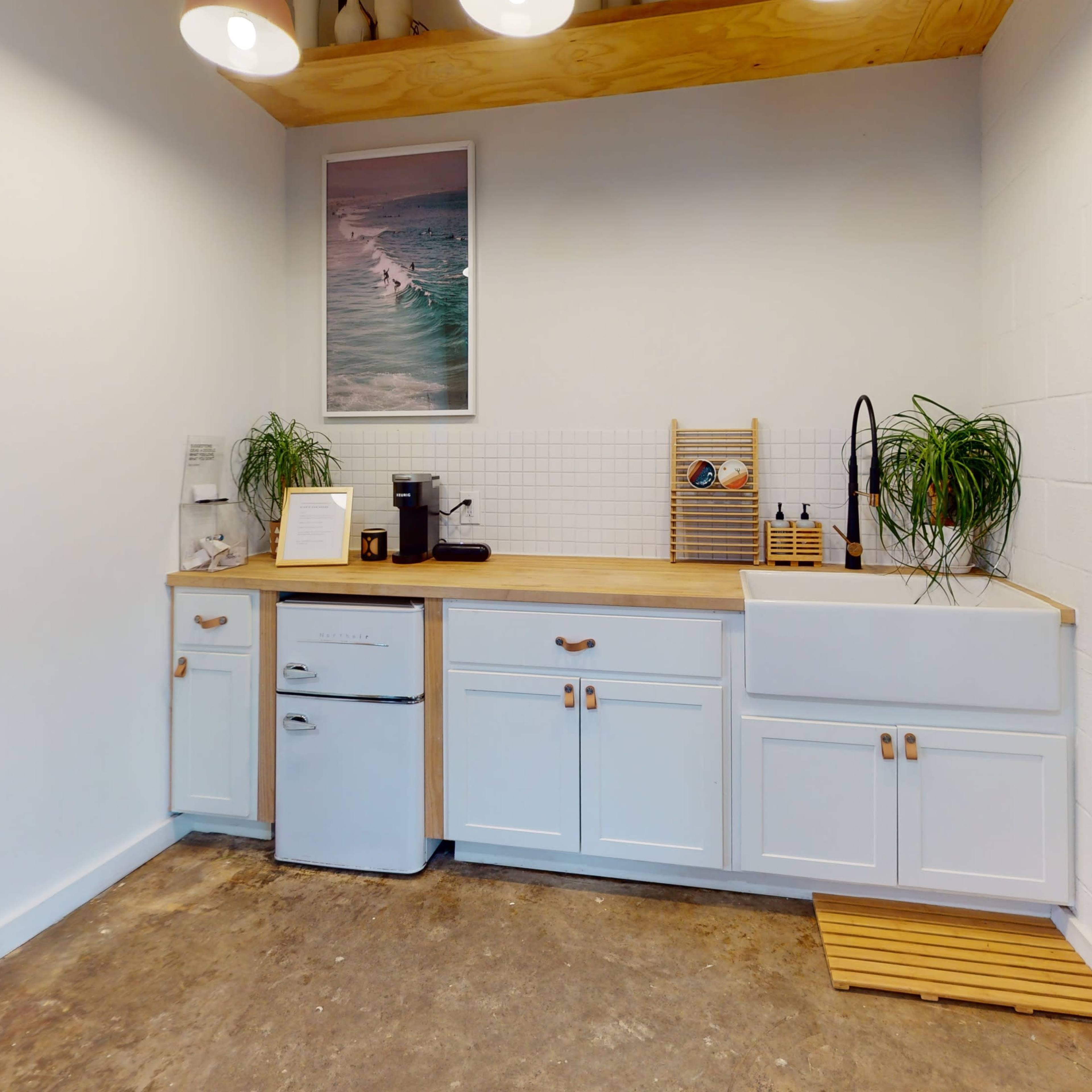 A kitchen area features a wooden countertop, white cabinets, and a vintage-style refrigerator, alongside plants and kitchen appliances.