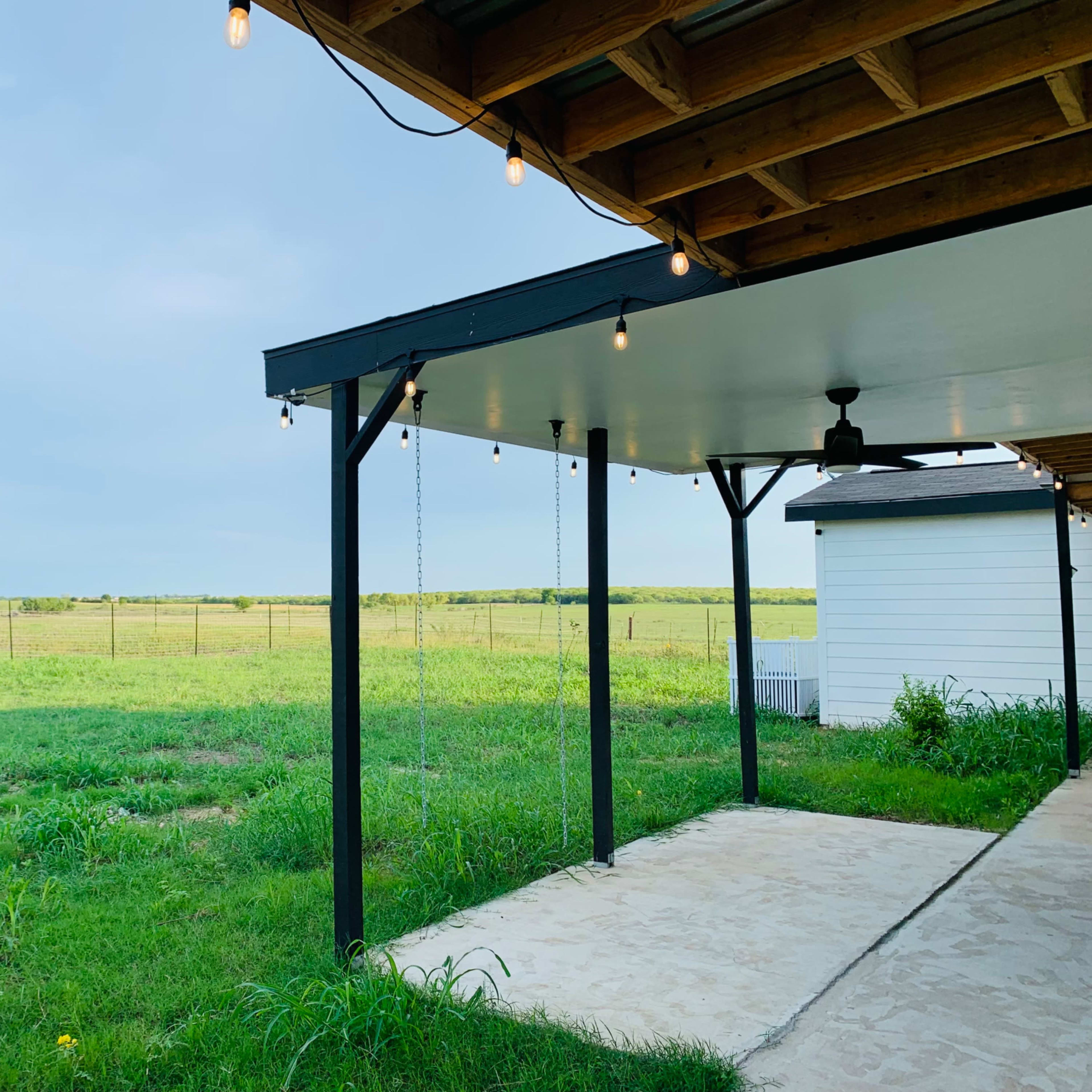 A covered patio with string lights overlooking a grassy field and a clear sky.