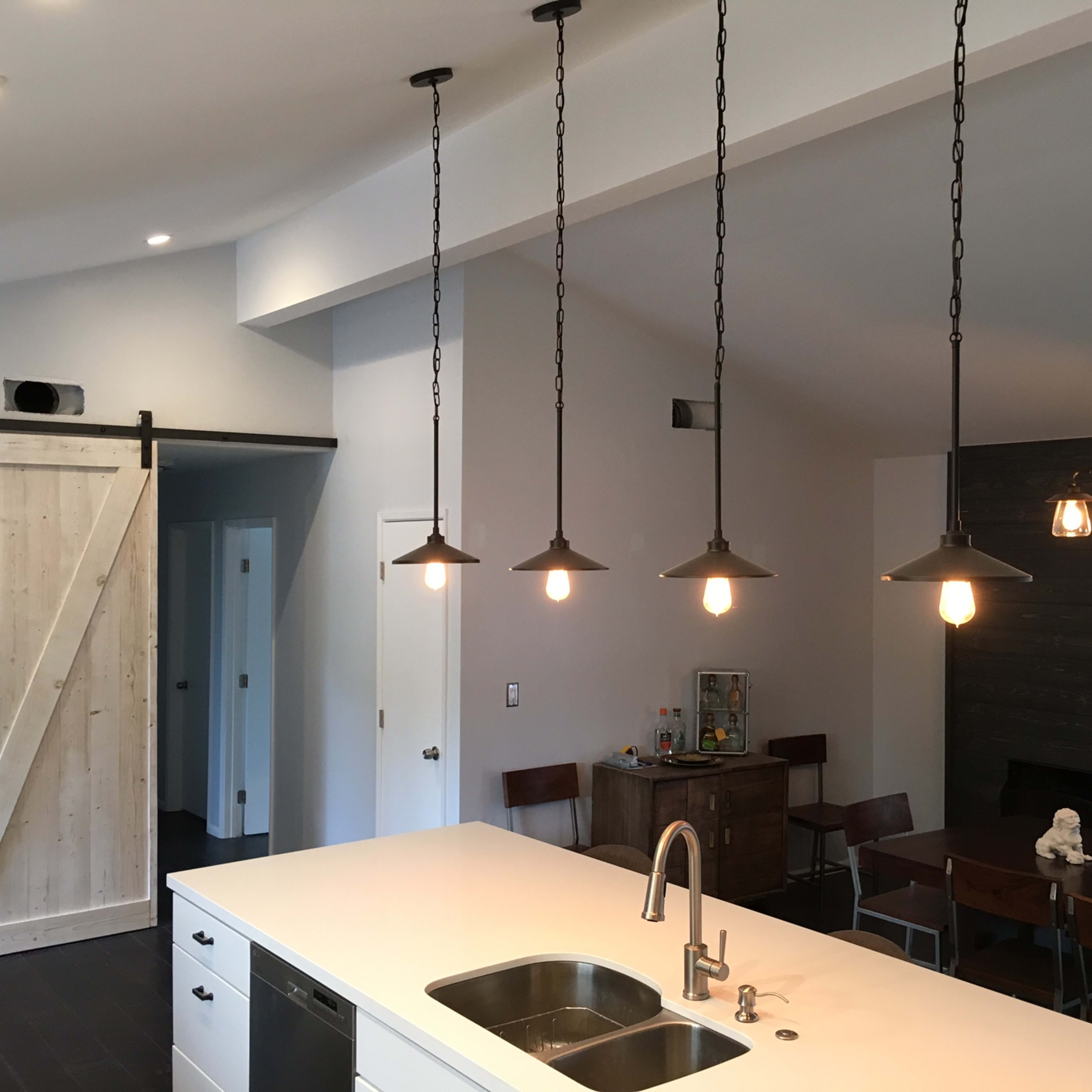 A modern kitchen features a large island with a double sink, pendant lighting, and a sliding barn door that leads to another room.