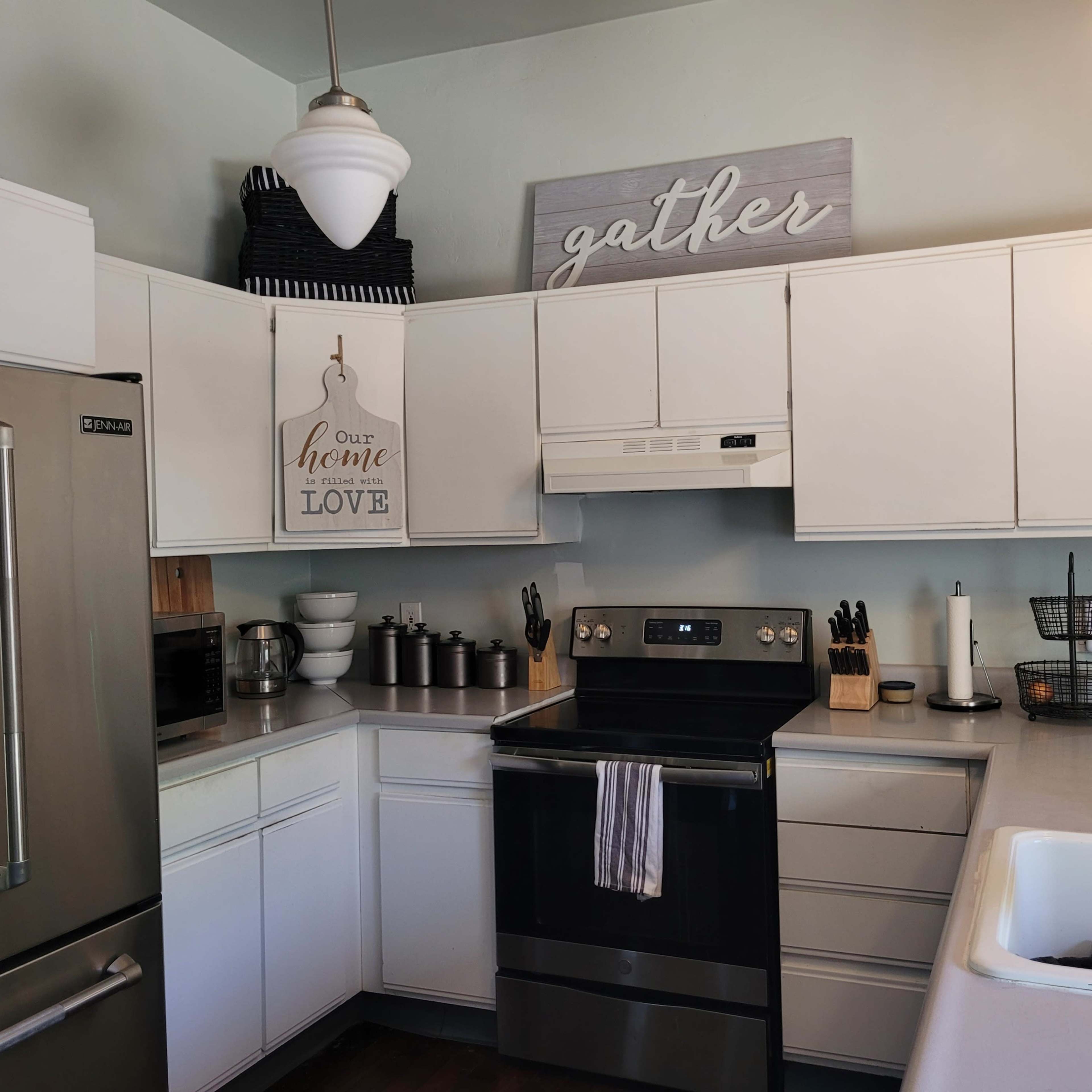A modern kitchen with white cabinetry, a black oven and stove, and decorative signs on the walls.