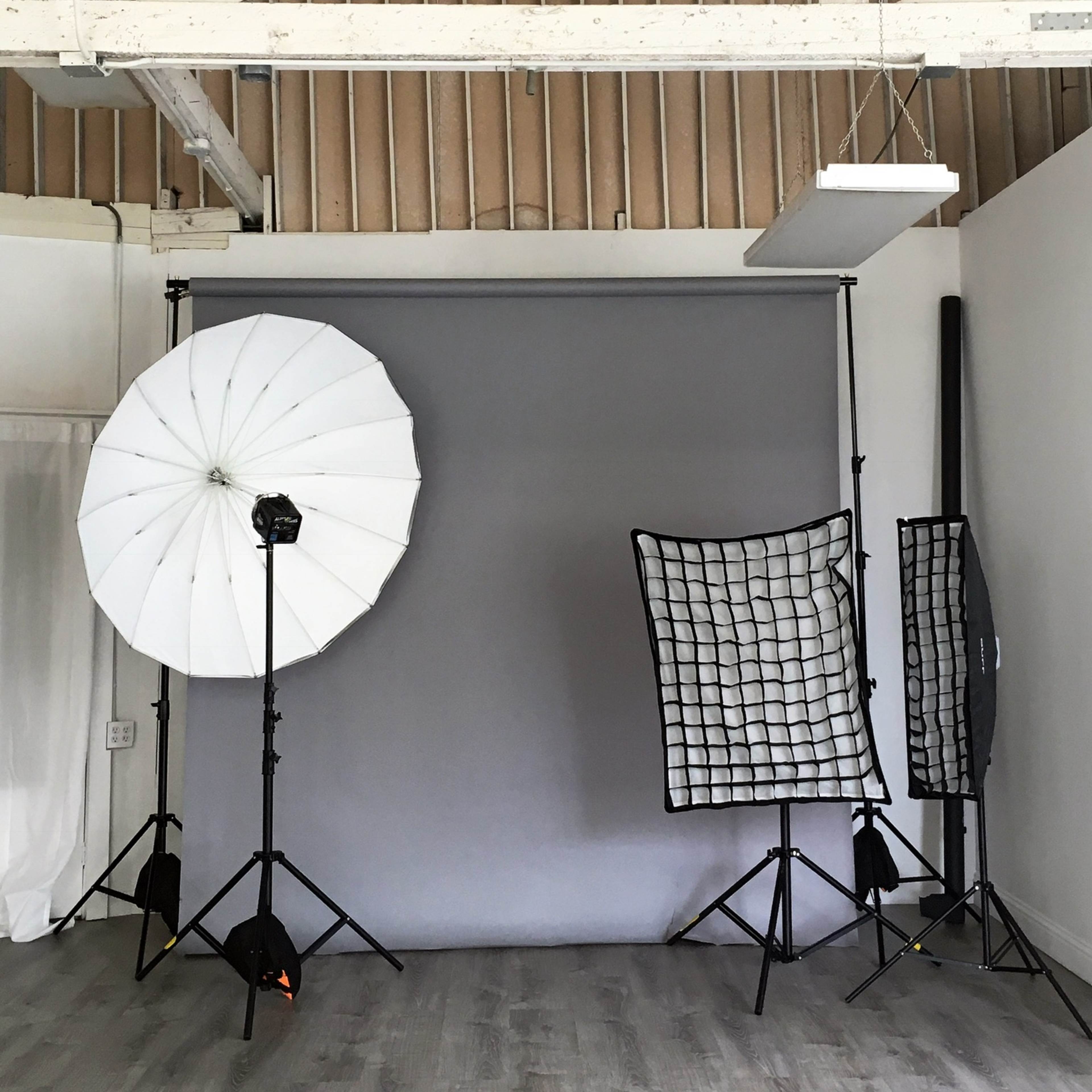 A photography studio with softbox lighting, a gray backdrop, and various light modifiers set up on a wooden floor.