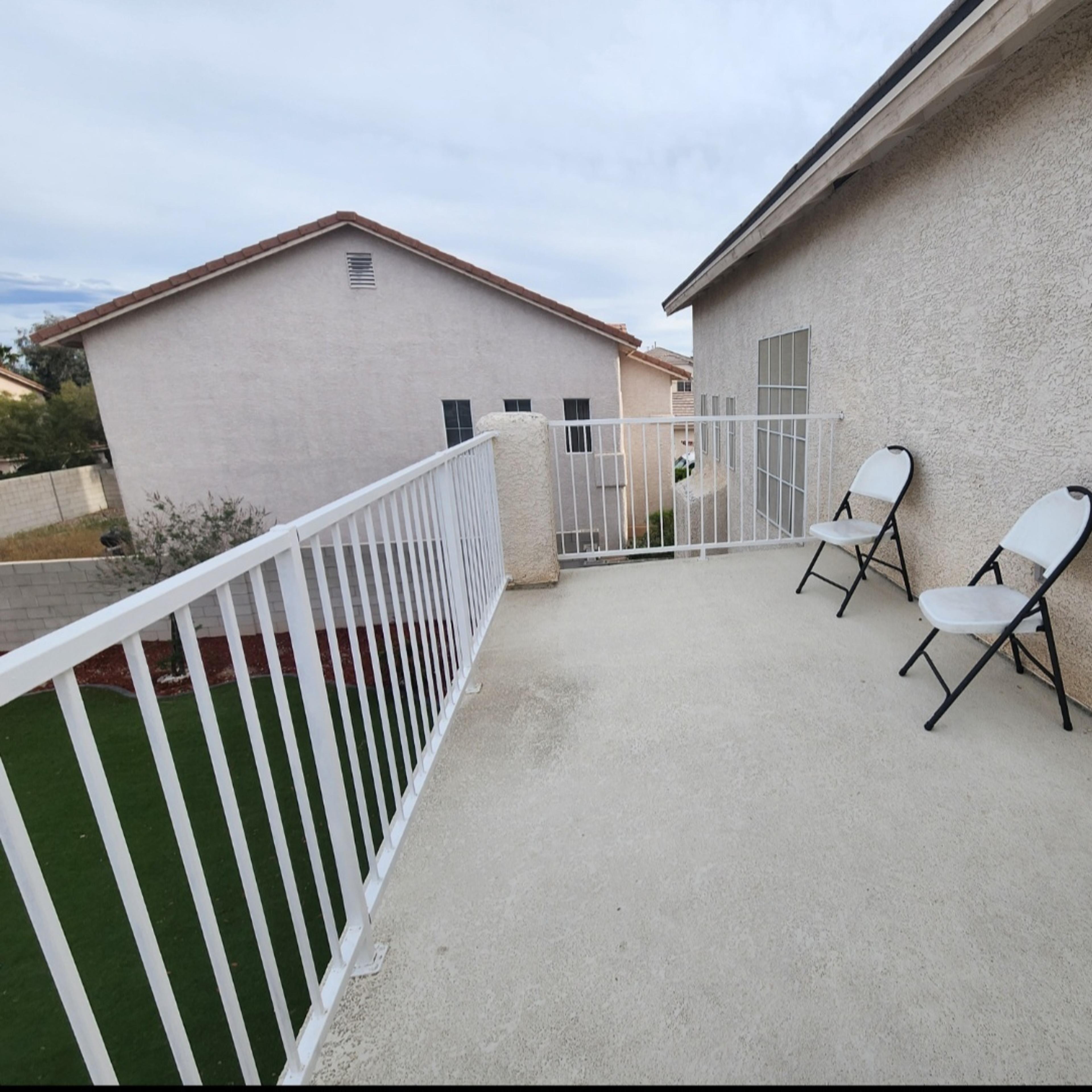 A small balcony with two white folding chairs and a view of adjacent houses.