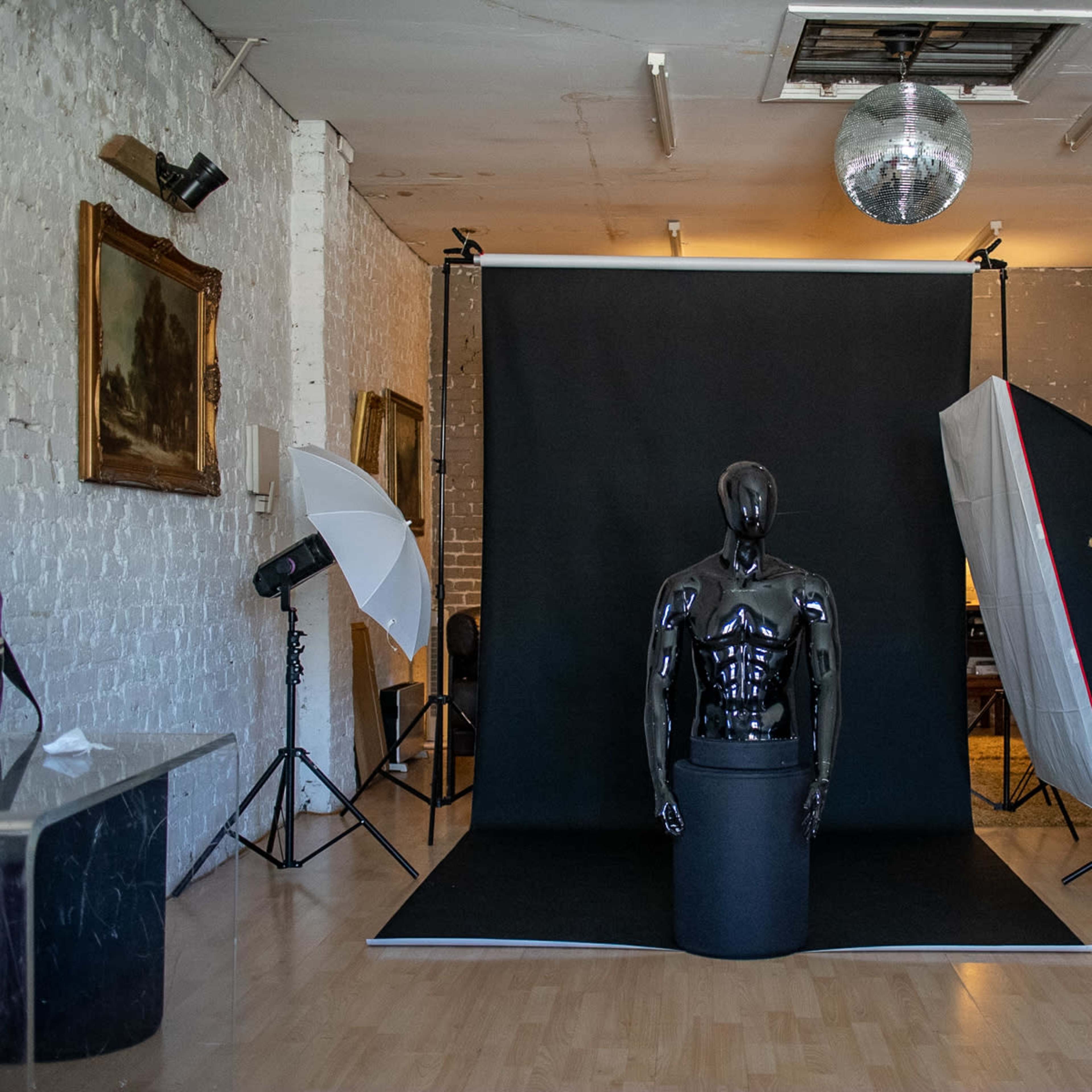 A photography studio setup with a black backdrop, a mannequin in a stand, and multiple lighting equipment arranged around the scene.