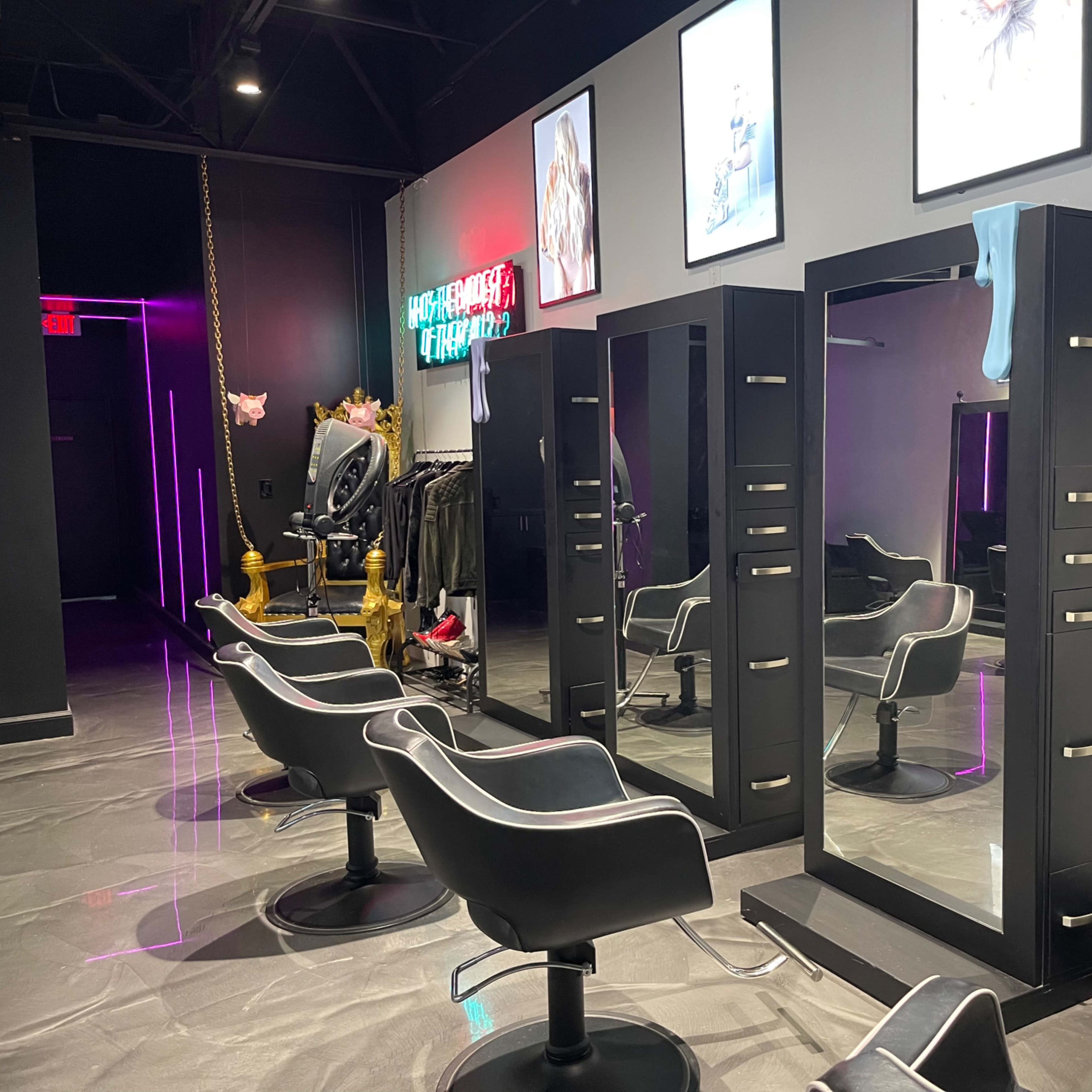 A modern hair salon with two styling stations, each equipped with a mirror and a black chair, adorned by framed art on the walls.