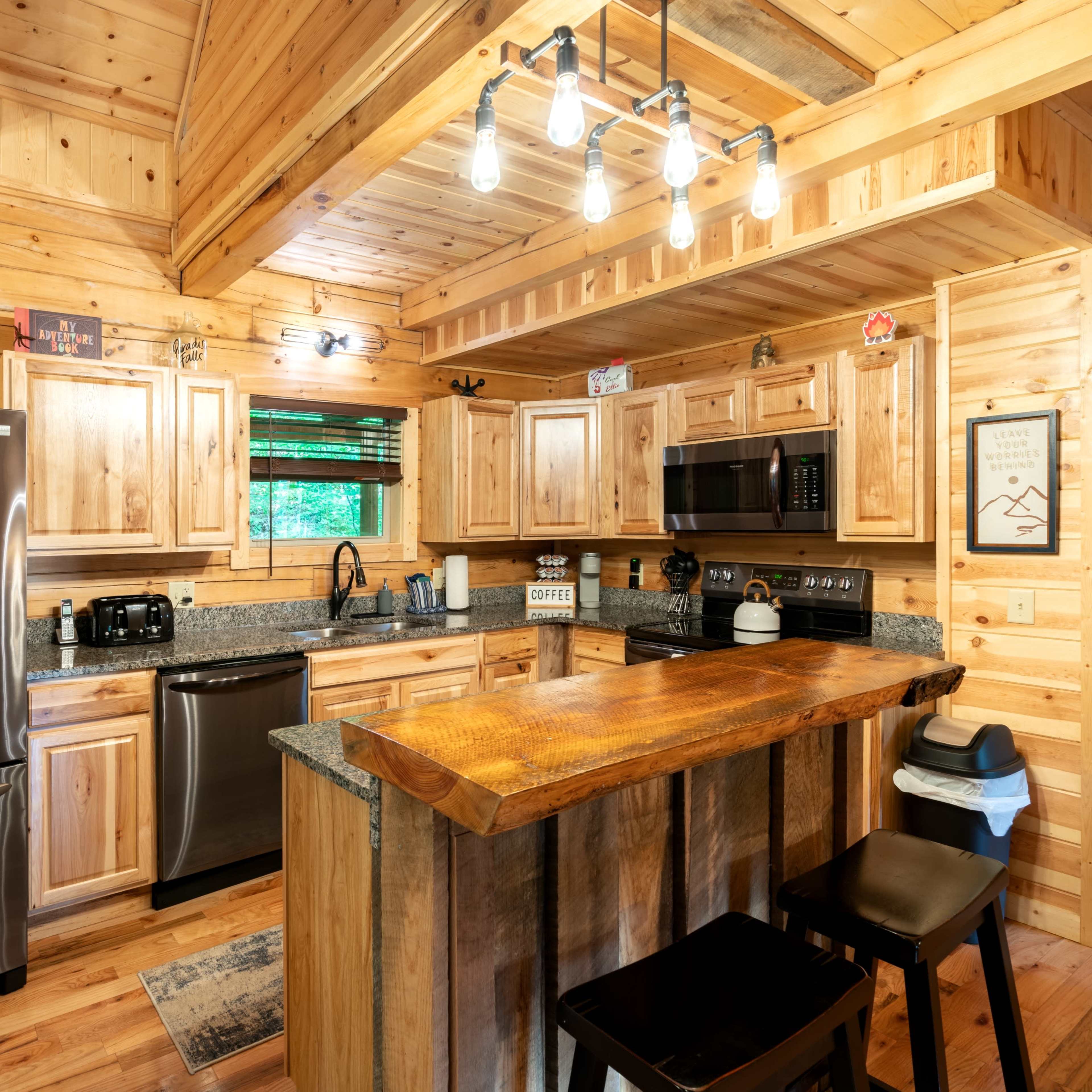A modern kitchen features wooden cabinets, a granite countertop, and stainless steel appliances, illuminated by pendant lights.
