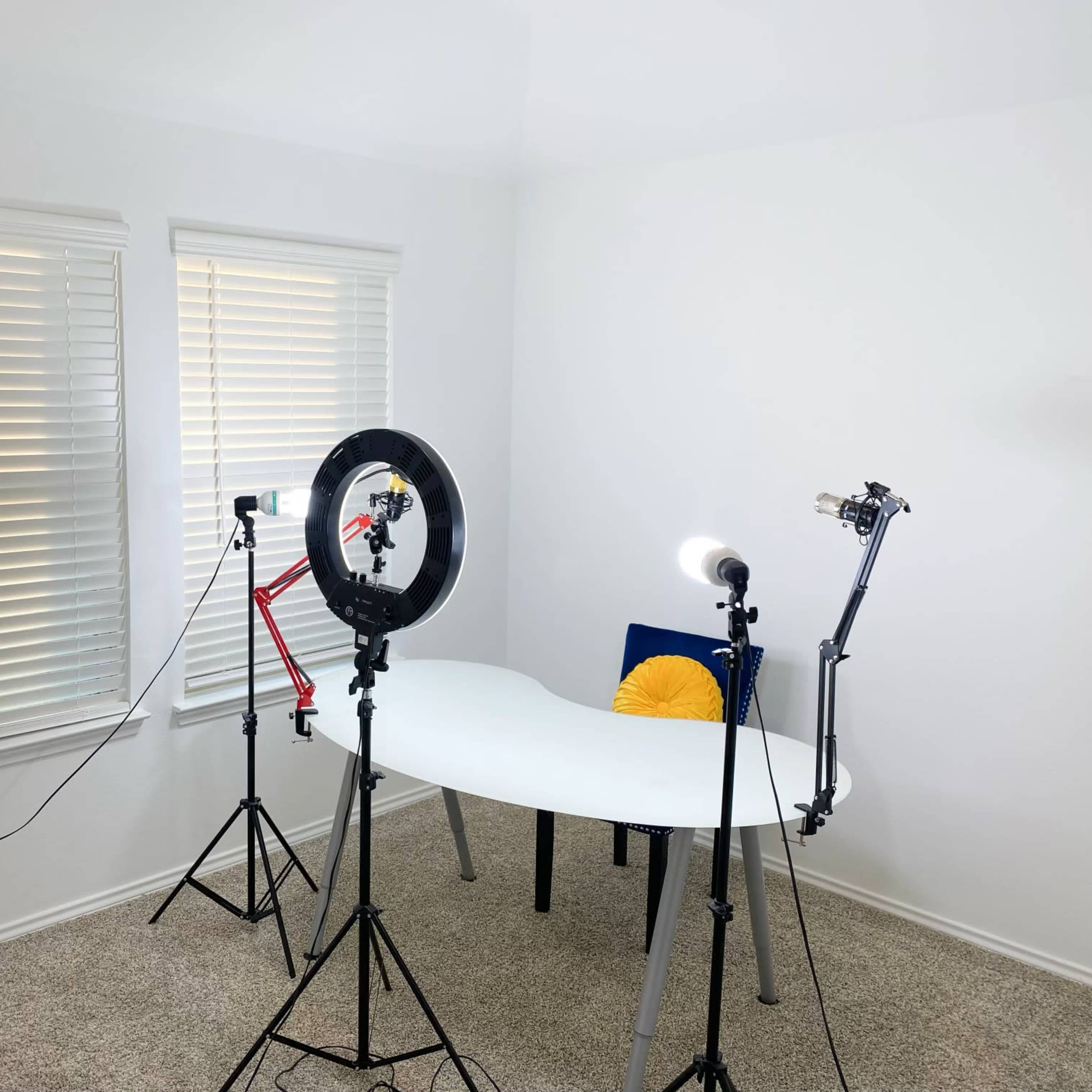 A bright, minimalistic room with a white table, a chair, and three lighting setups positioned around it.