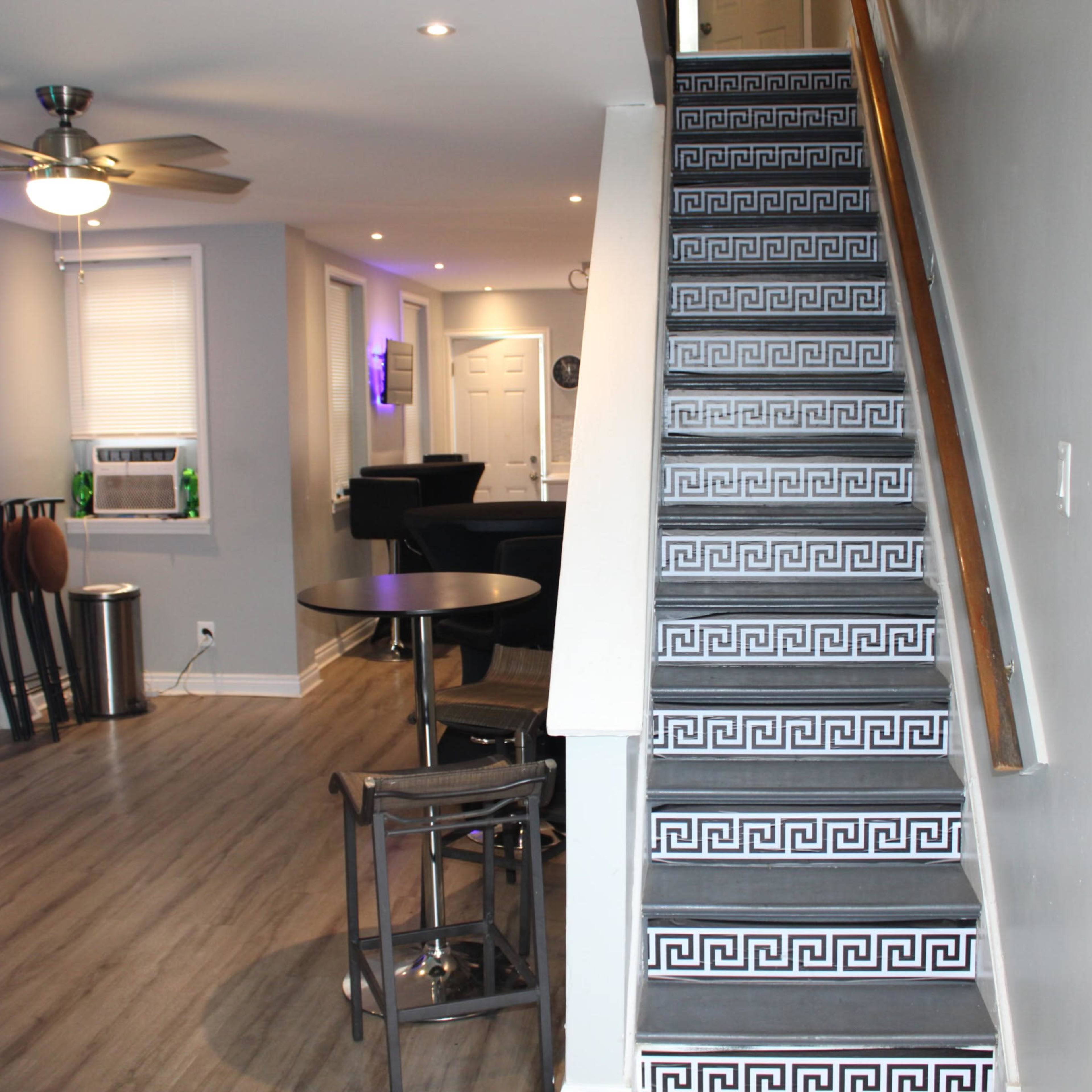 A modern interior with a staircase featuring patterned risers, leading to a living area with a seating arrangement and a wall-mounted television.
