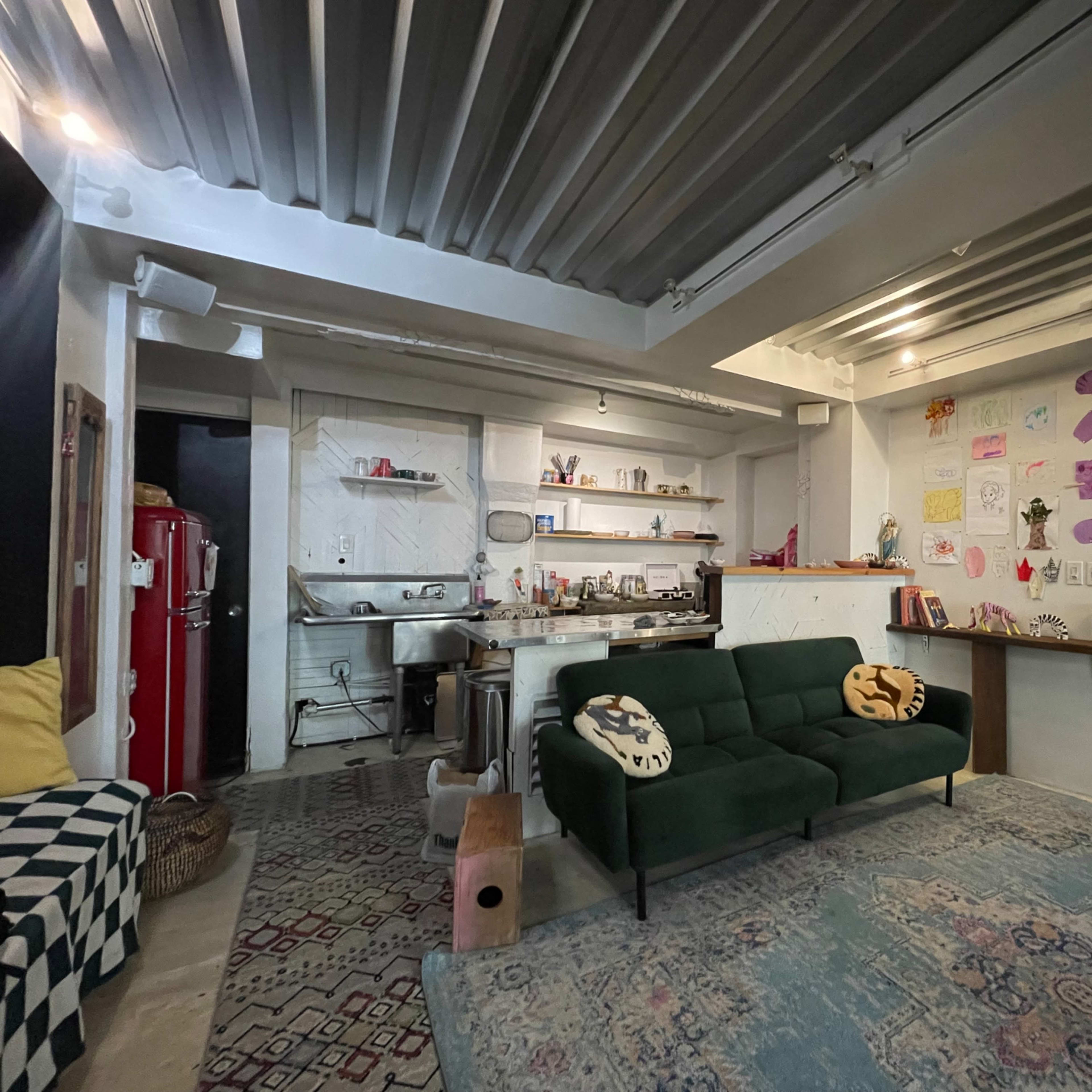 A modern living space with a green sofa, an open kitchen area, and colorful artwork on the walls.