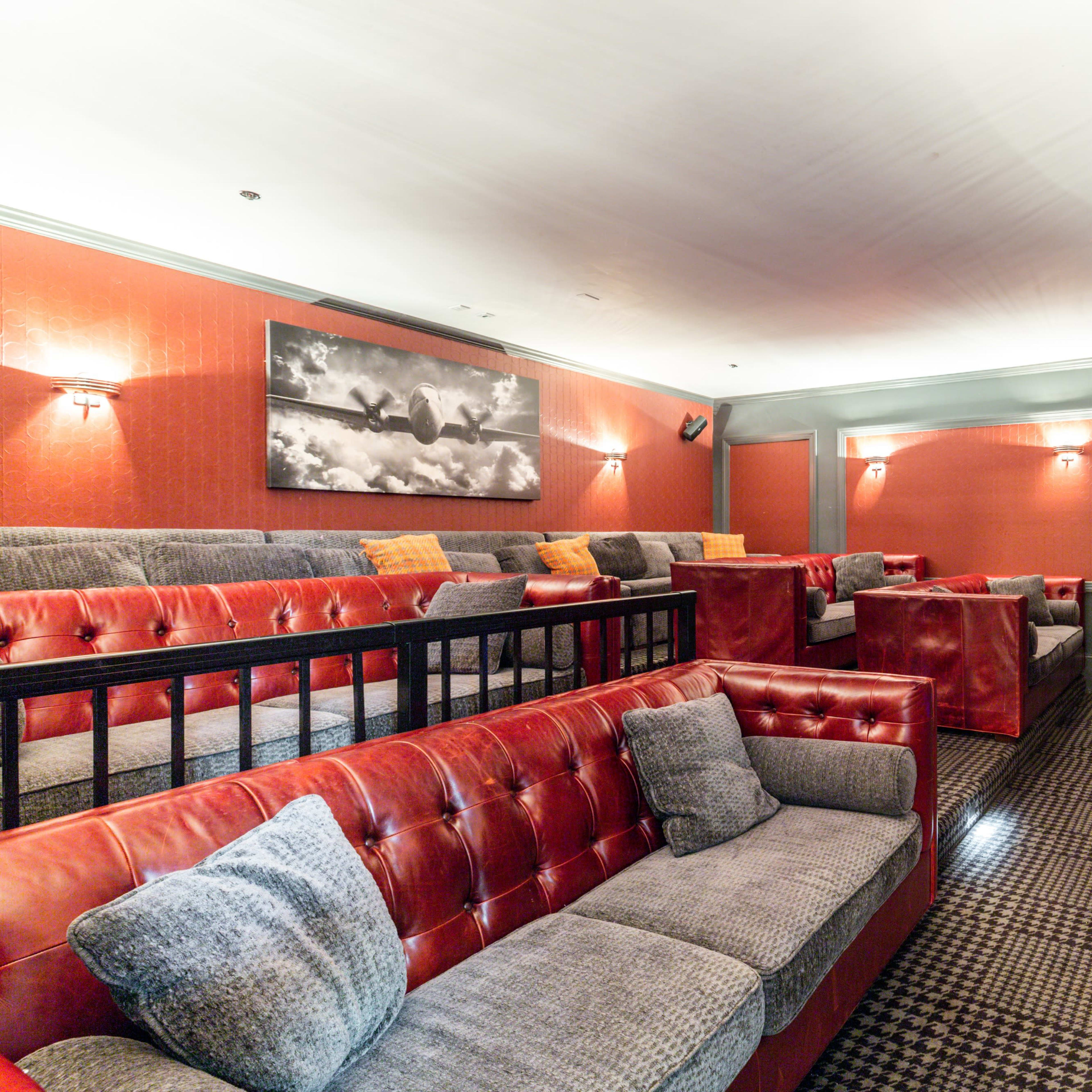 A home theater with red walls, plush seating arranged in tiers, and a large screen mounted on one wall.