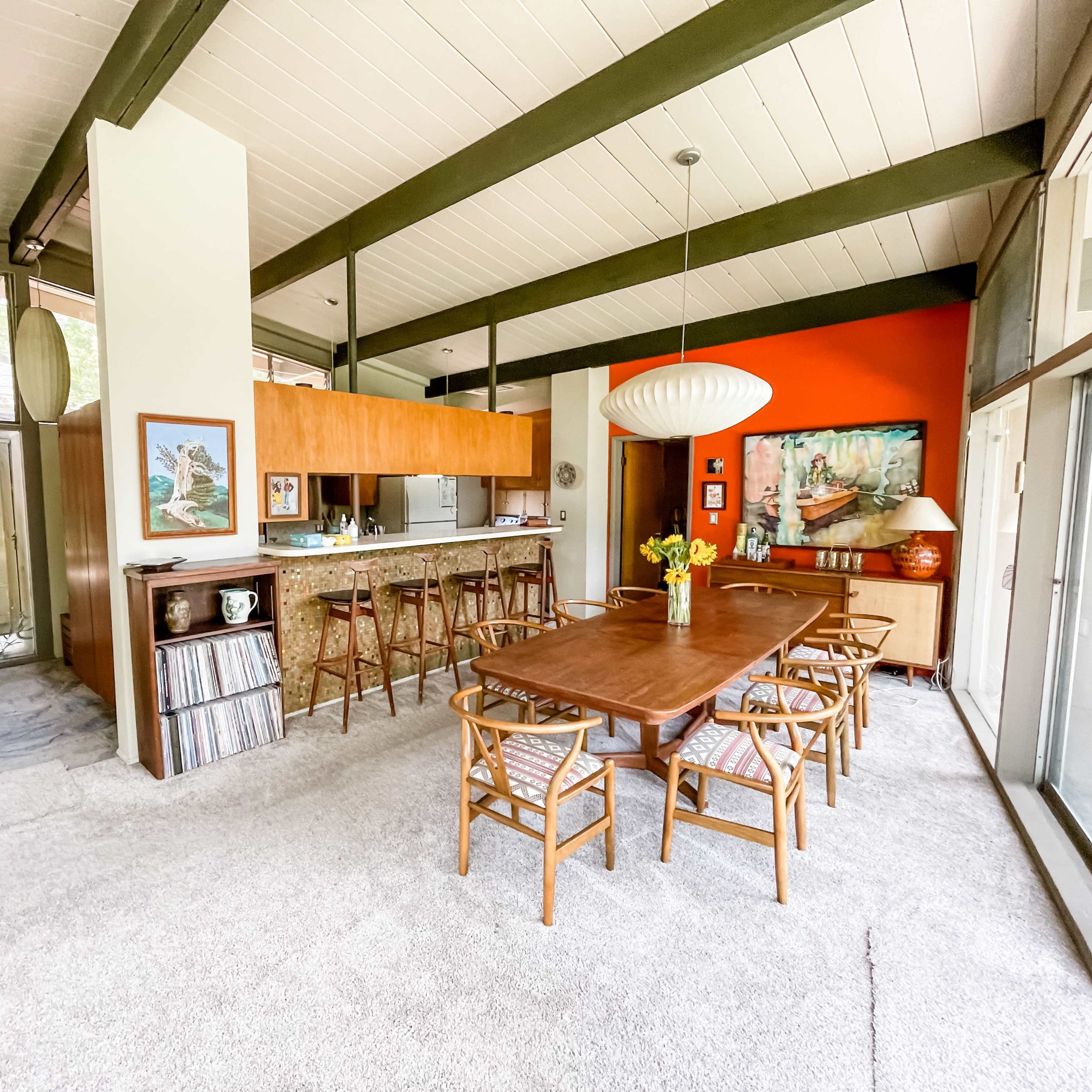 A mid-century modern dining area with a long wooden table, rattan chairs, and a vibrant accent wall.