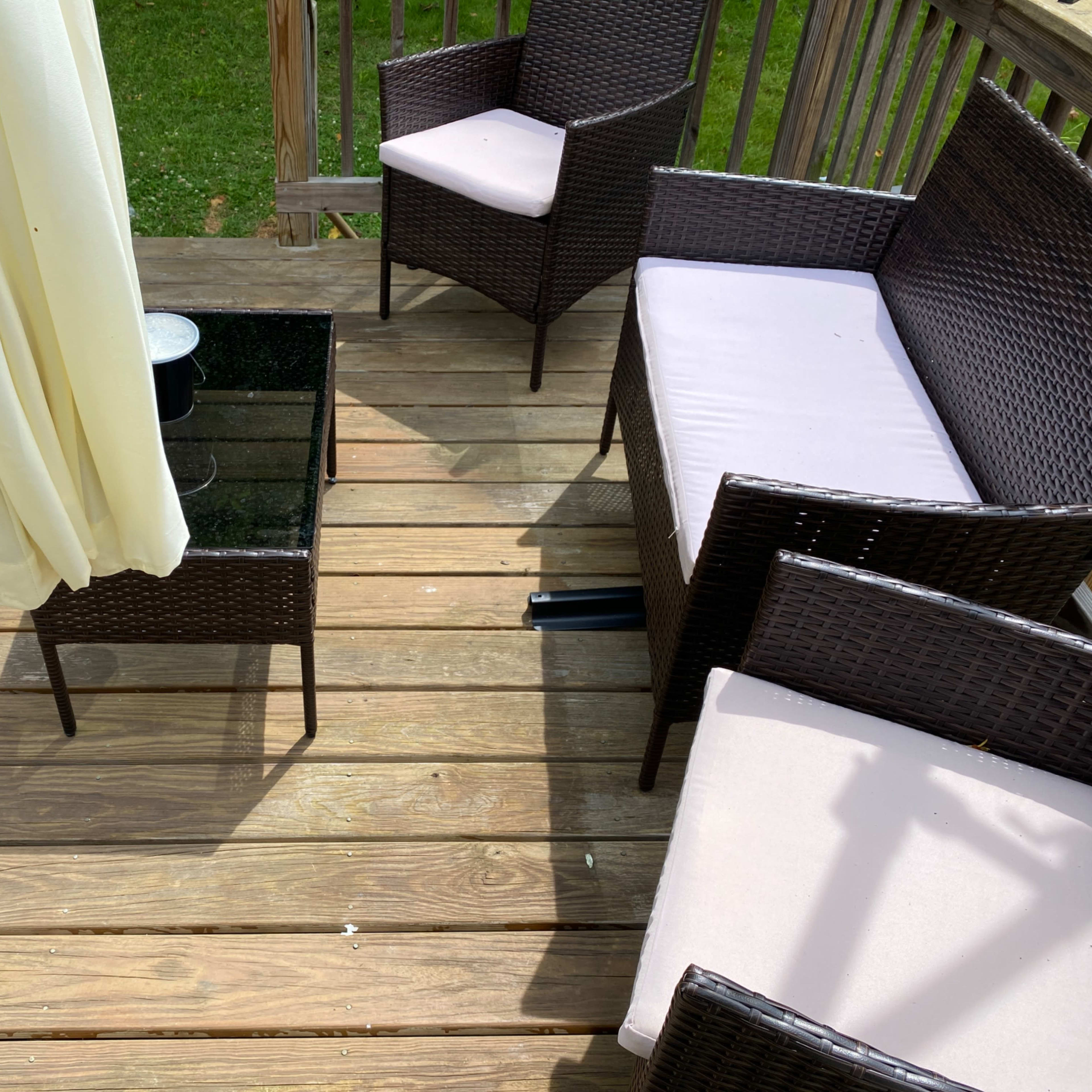A patio area features a wooden deck with two wicker chairs, a small glass-top table, and a yellow umbrella partially open.