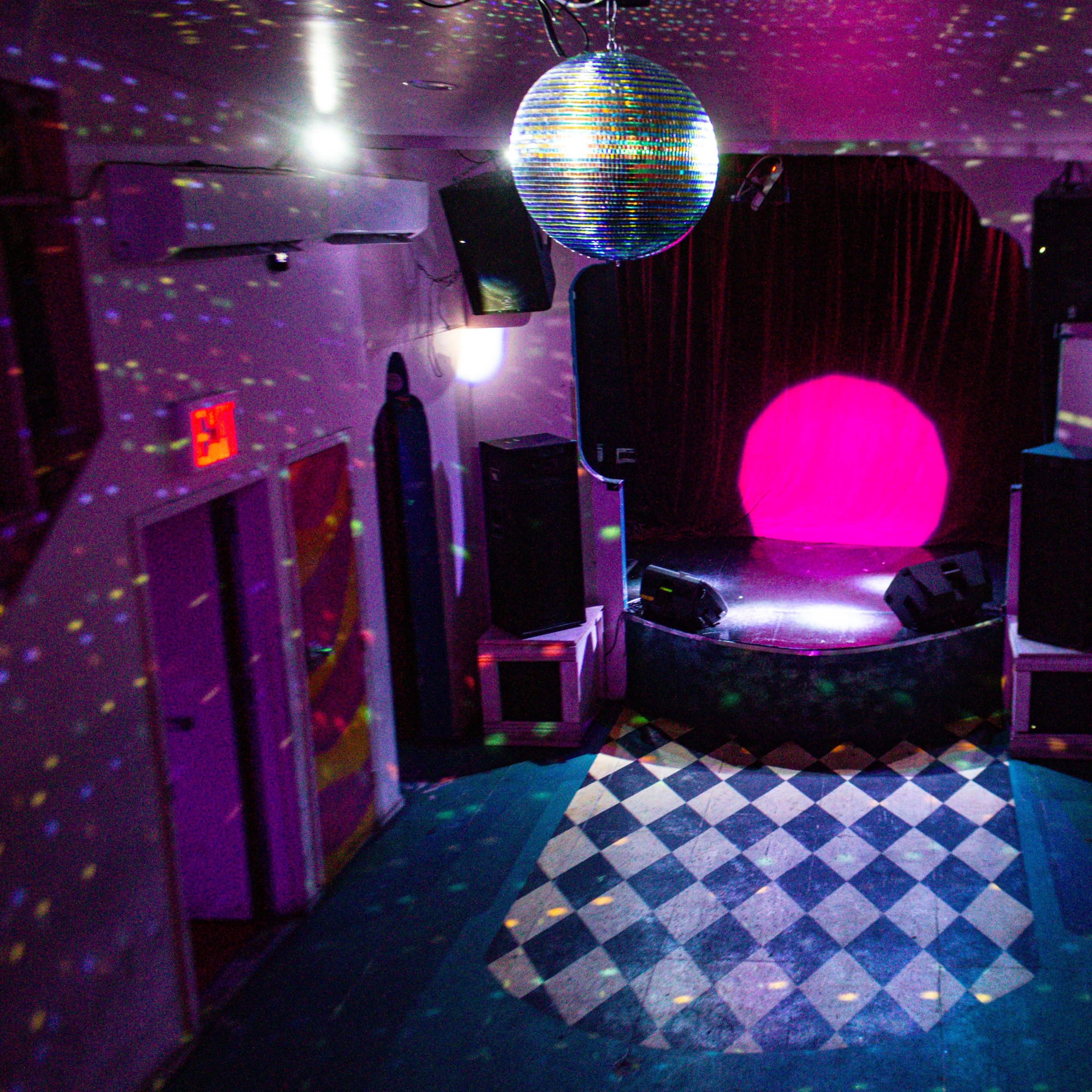 An empty performance space with a circular stage, colorful lights reflecting off the walls, and a disco ball hanging from the ceiling.