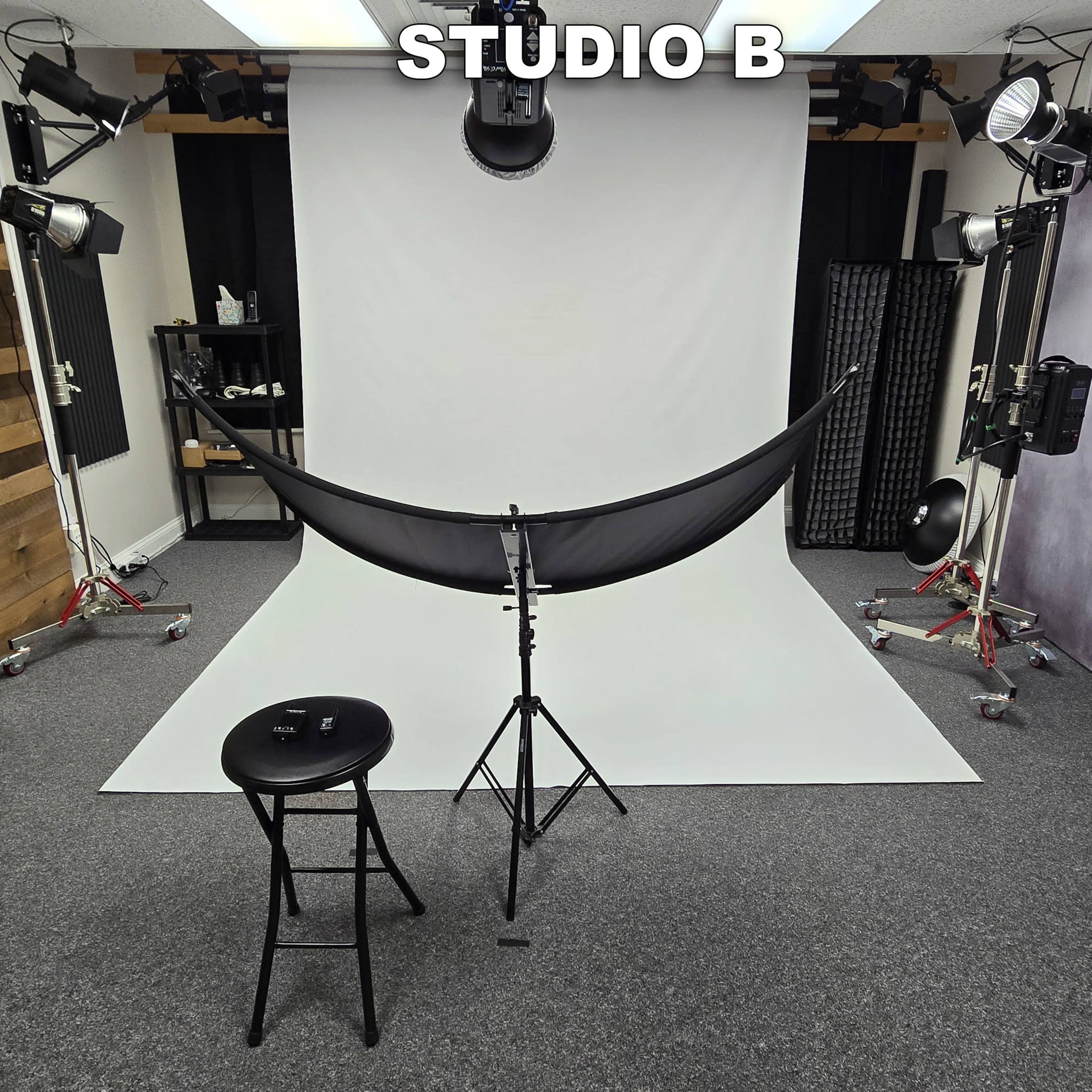 A photography studio with a white backdrop, a black fabric draped on a stand, and various lighting equipment arranged around the space.