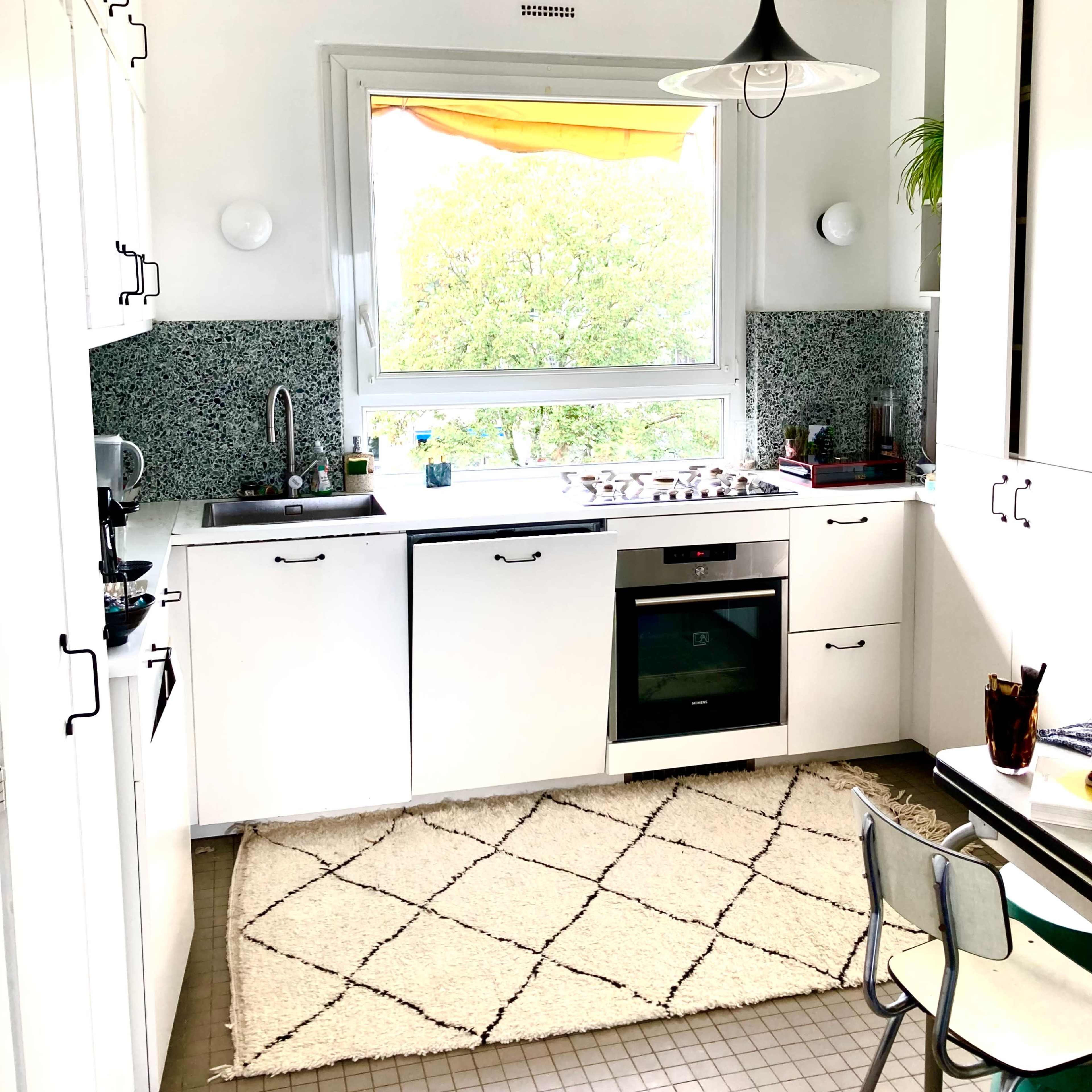 A modern kitchen features white cabinetry, a stove and oven, and a window overlooking greenery.