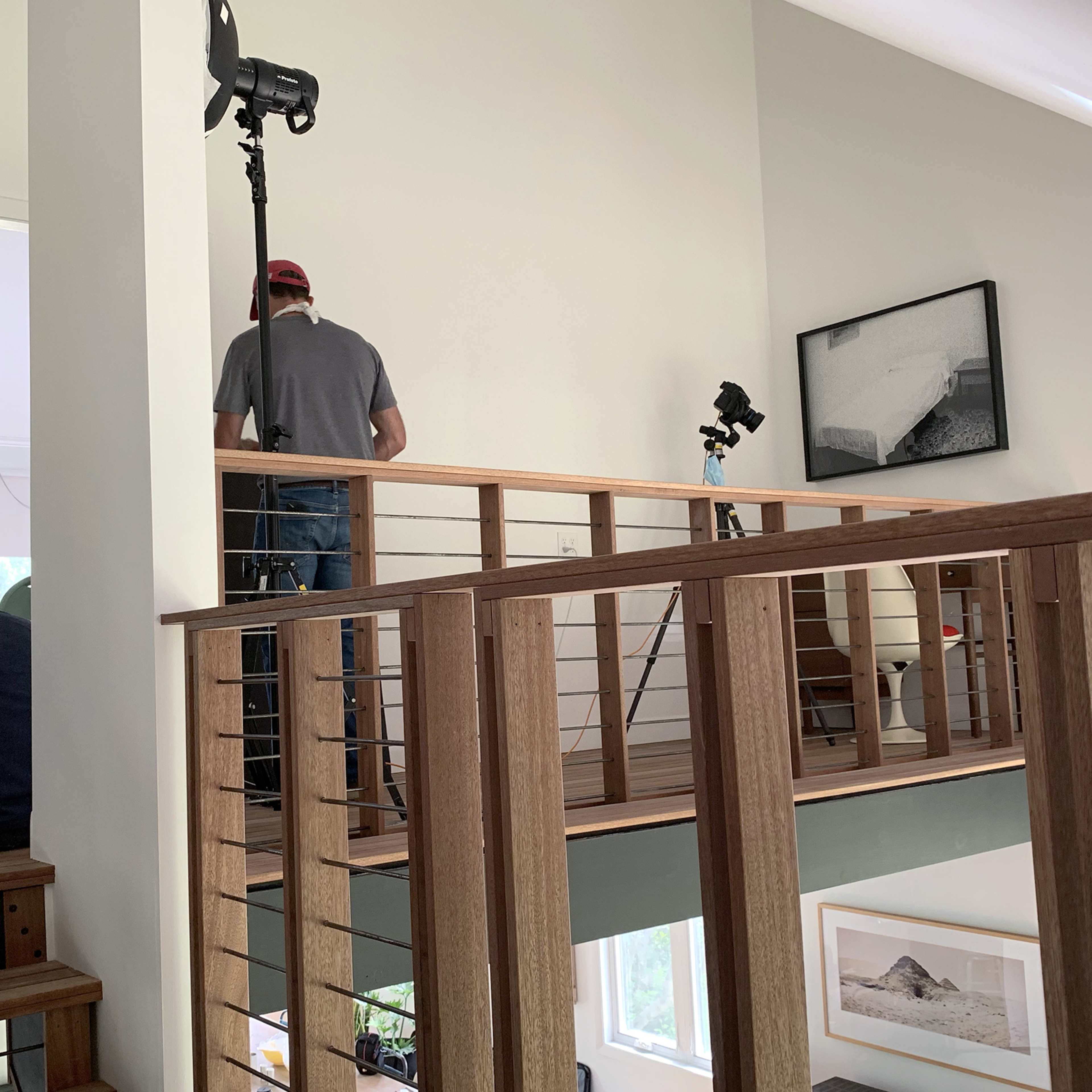 Two people are working on a staircase in a well-lit interior space, next to a large cartoon-style sign on the wall and several lights positioned for a shoot.