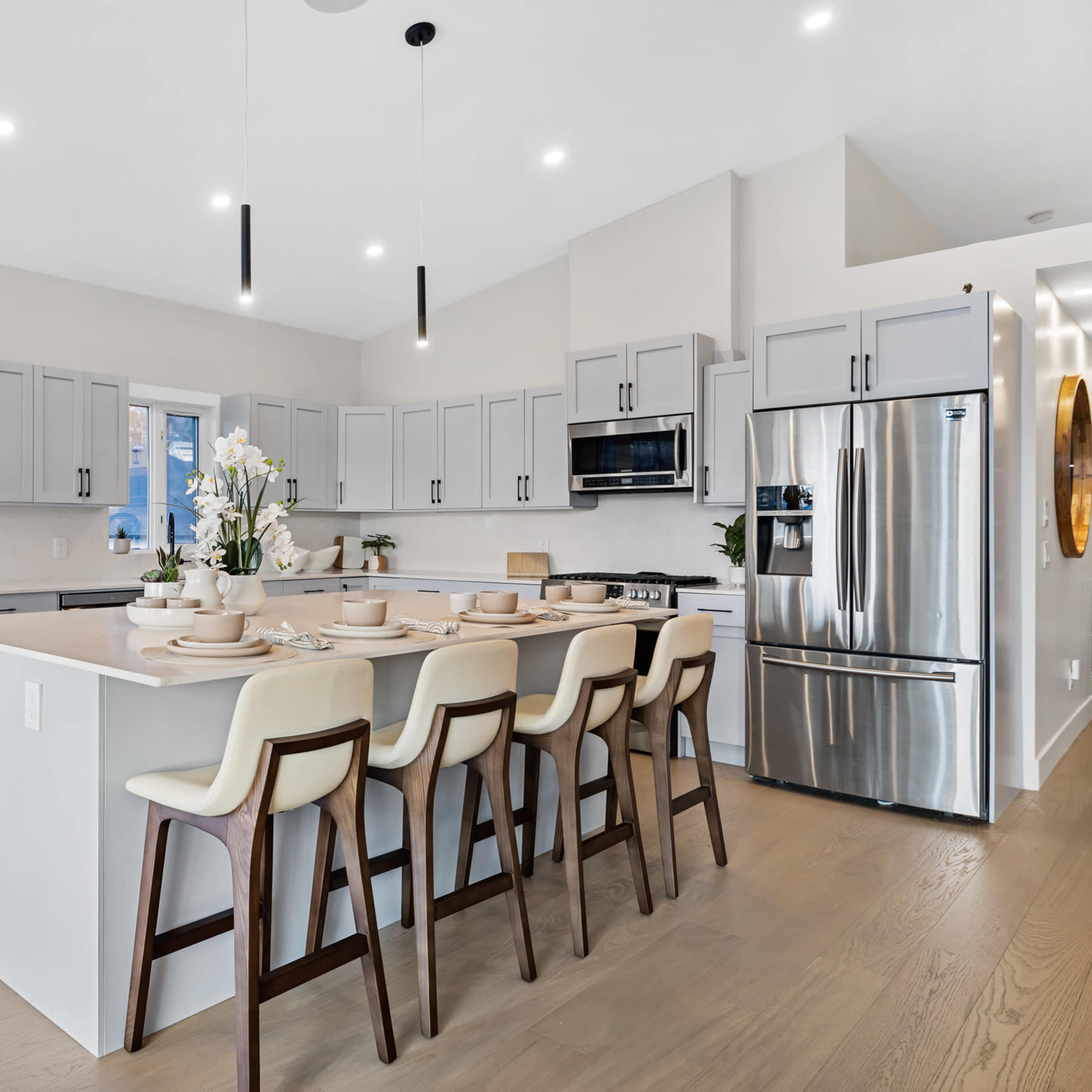 A modern kitchen features a large central island with seating, gray cabinets, and stainless steel appliances.