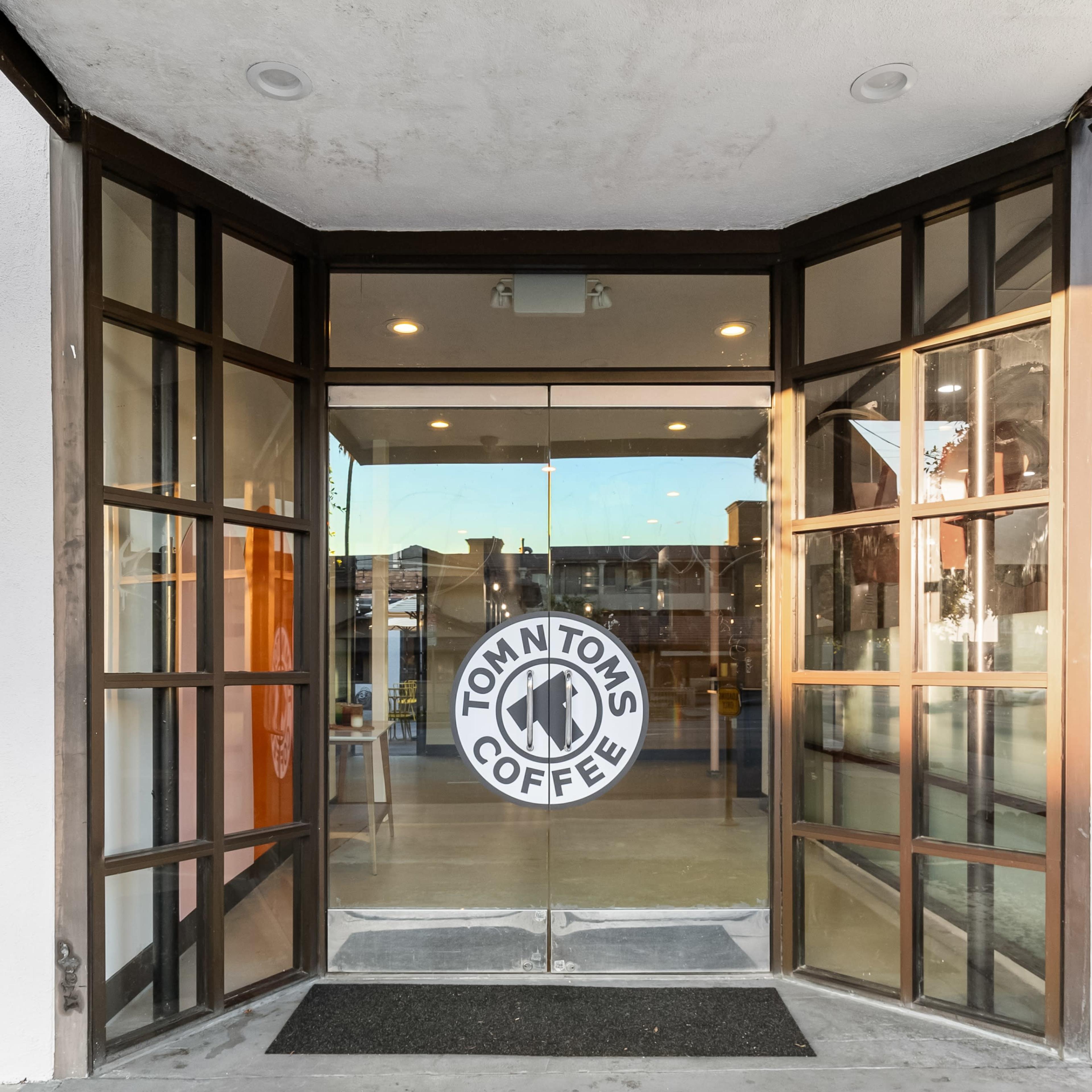 The entrance of a coffee shop with glass double doors featuring a round logo that reads "Tom N Toms Coffee."