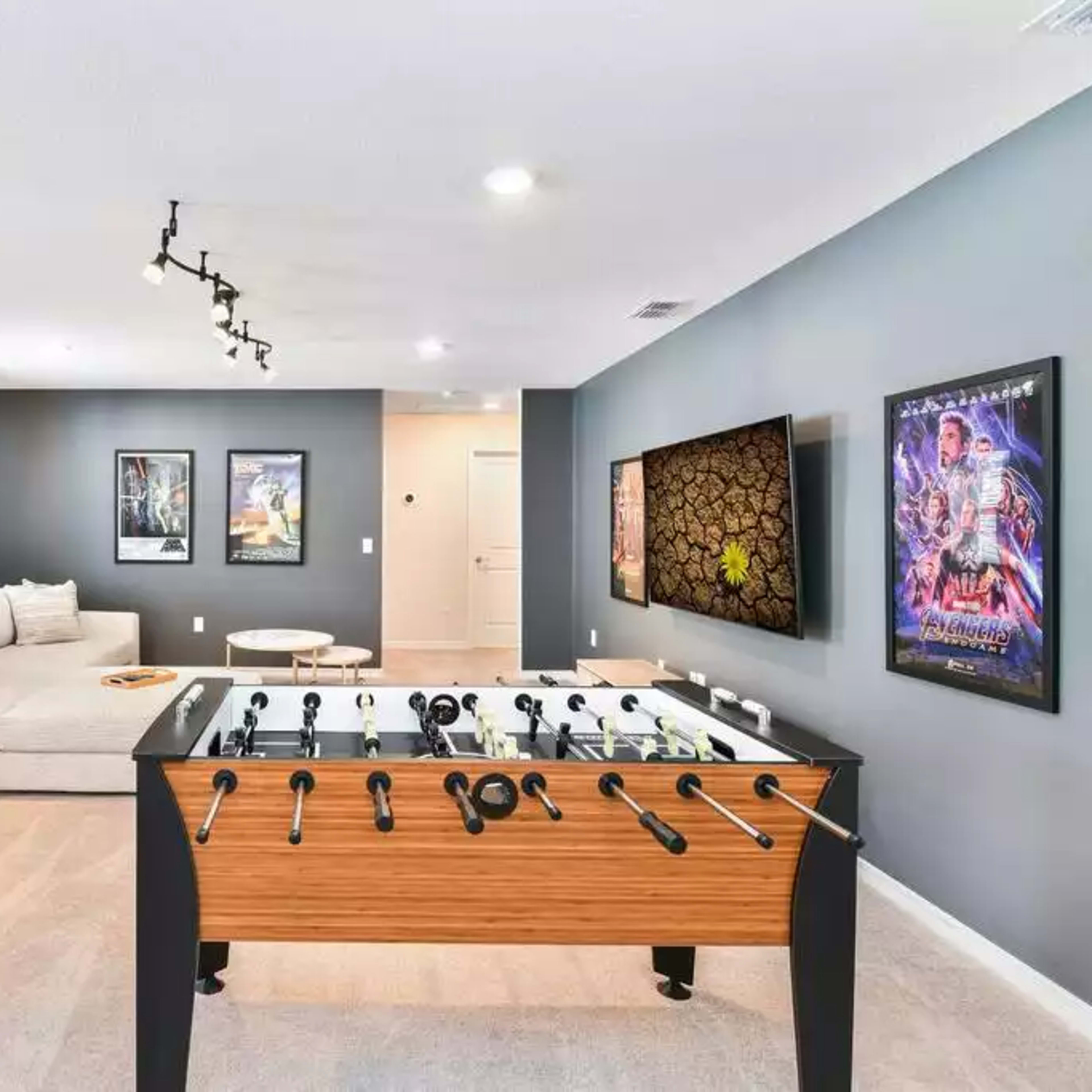 A game room featuring a large sectional couch, a foosball table, and movie posters on the walls.
