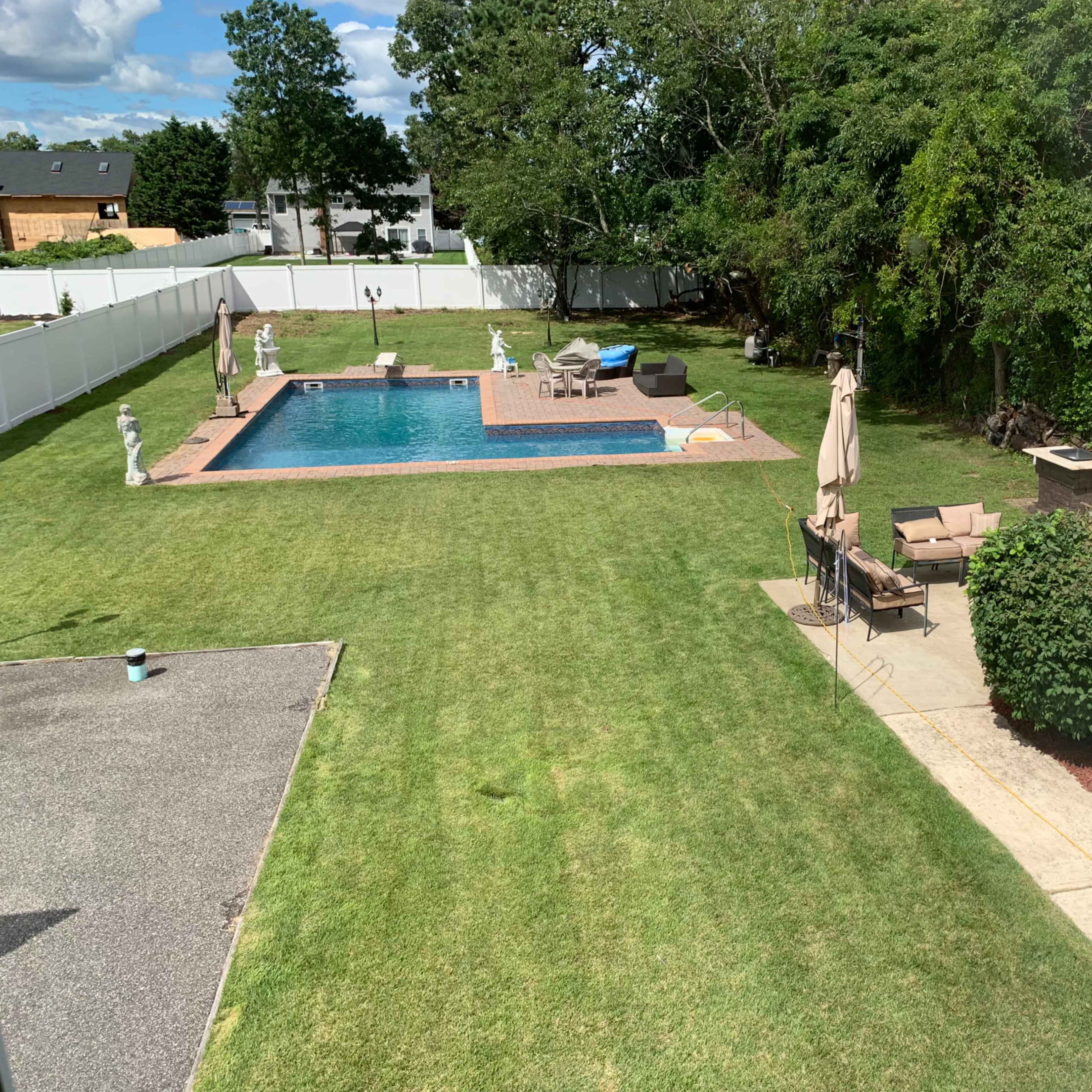 A backyard with a swimming pool, landscaped grass, garden furniture, and decorative statues.