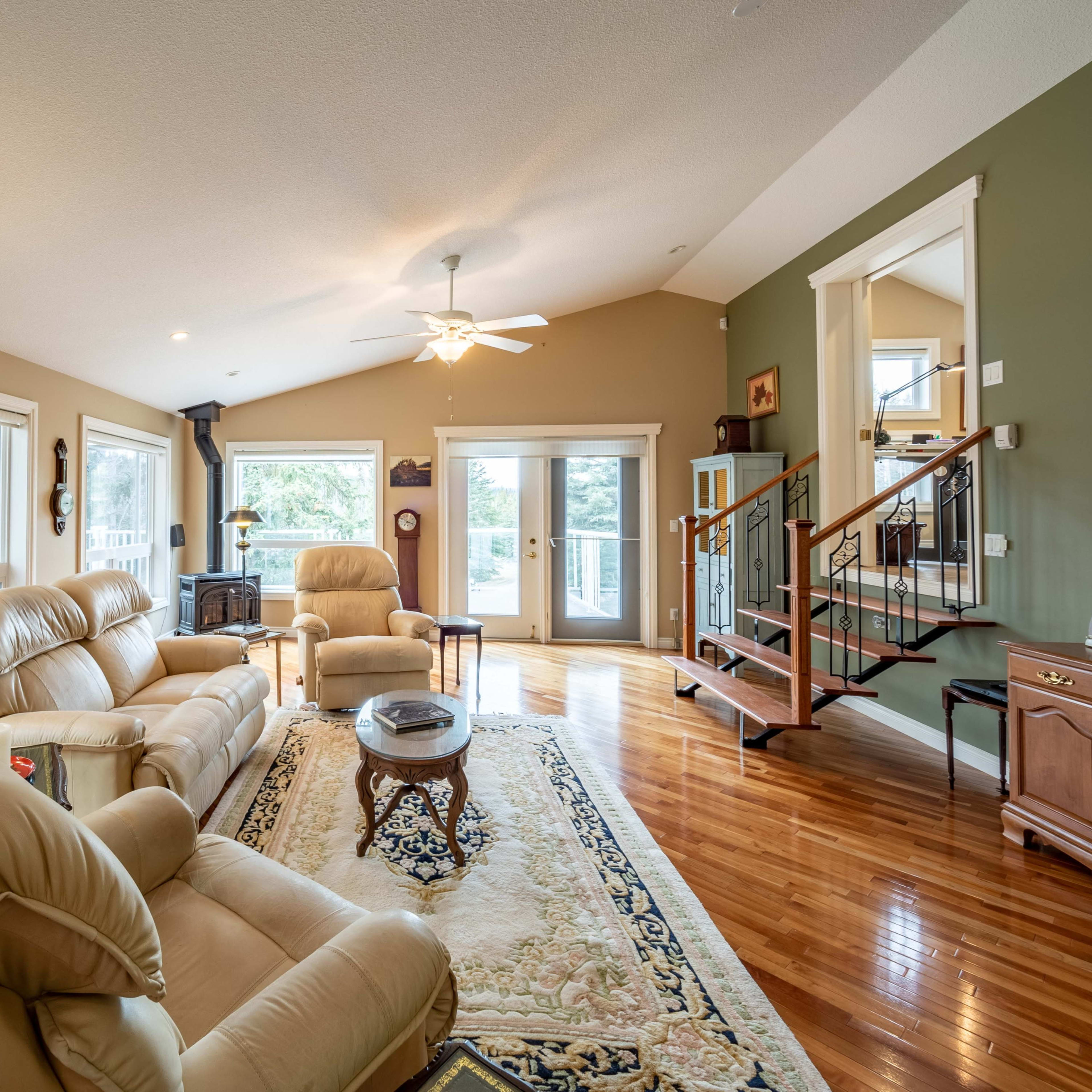 The living room features light-colored leather seating, hardwood flooring, and large windows that allow natural light to fill the space.