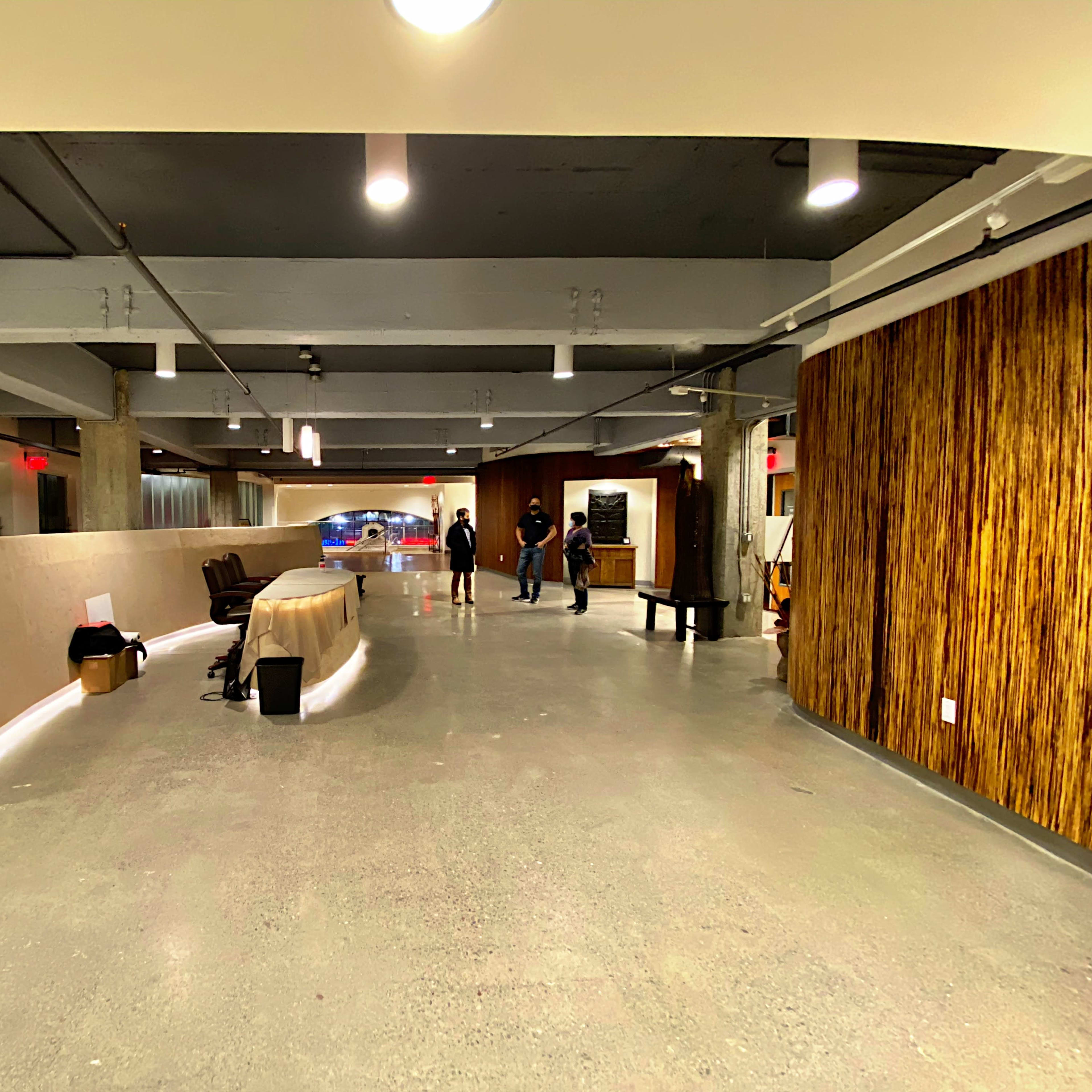 A spacious, modern lobby area featuring a smooth concrete floor, a curved reception desk, and several people gathered in conversation.