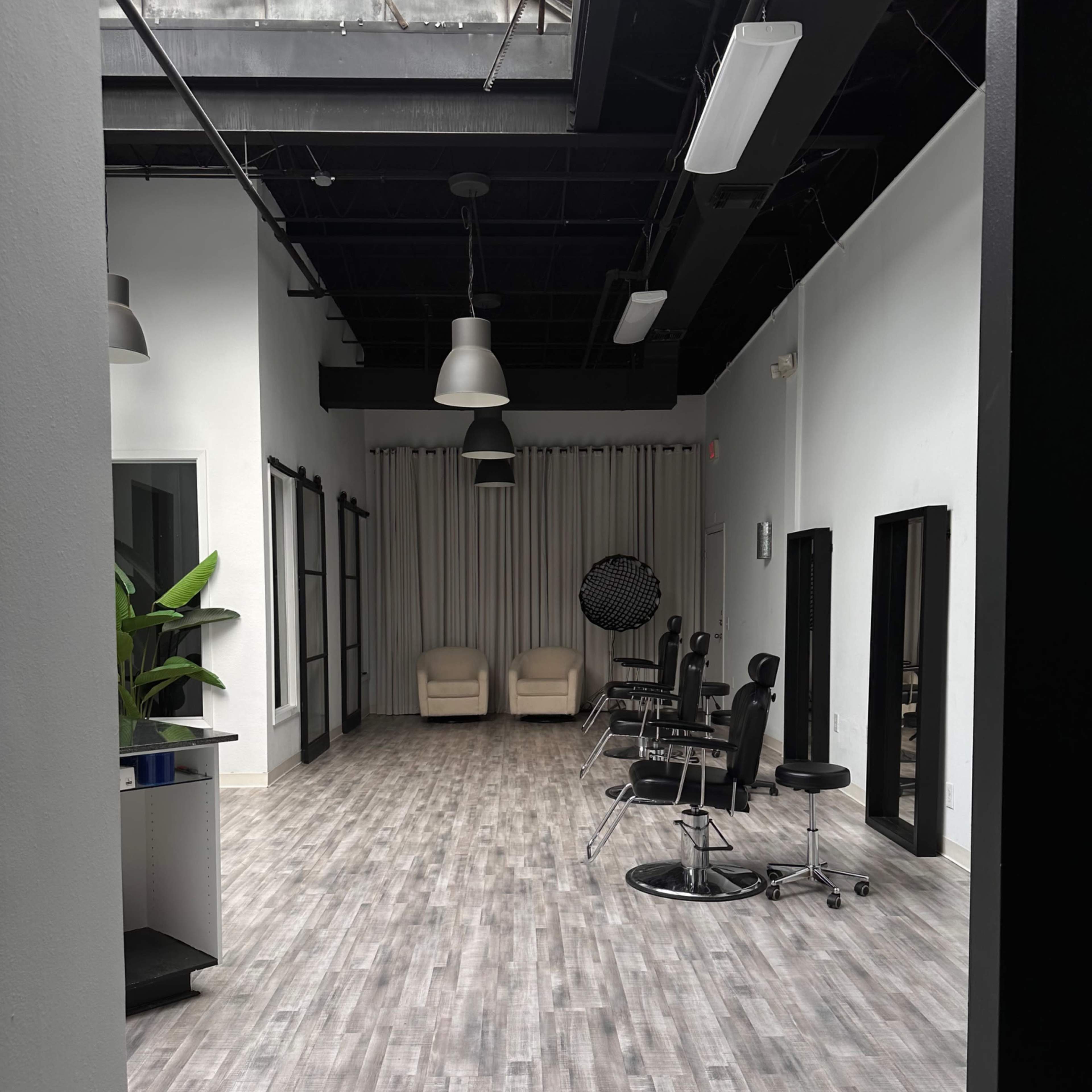 A spacious, modern interior with light wood flooring, two chairs at the far end, and several salon-style chairs along one side.