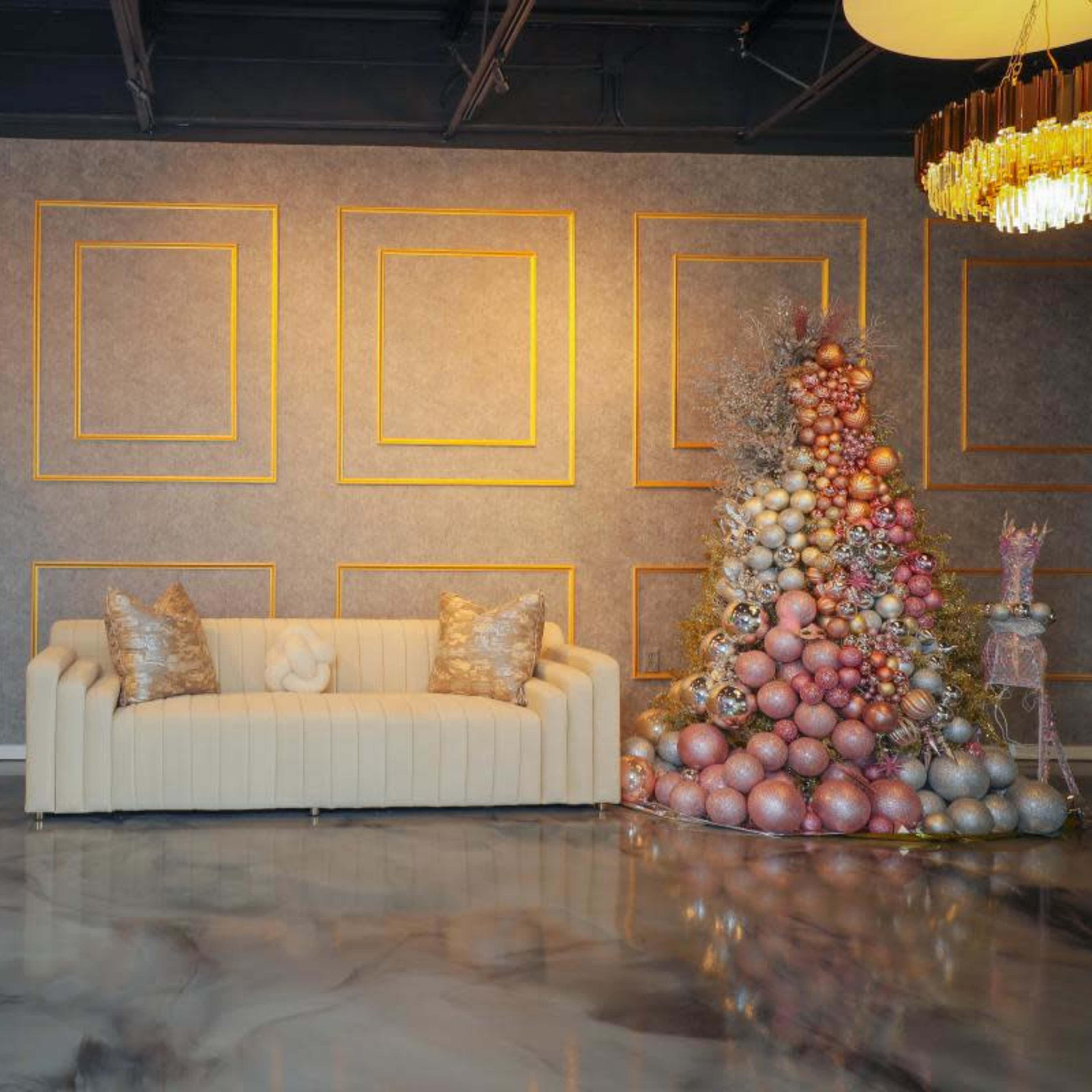 A modern living space features a beige couch, a decorative wall with gold-framed panels, and a colorful Christmas tree adorned with ornaments.