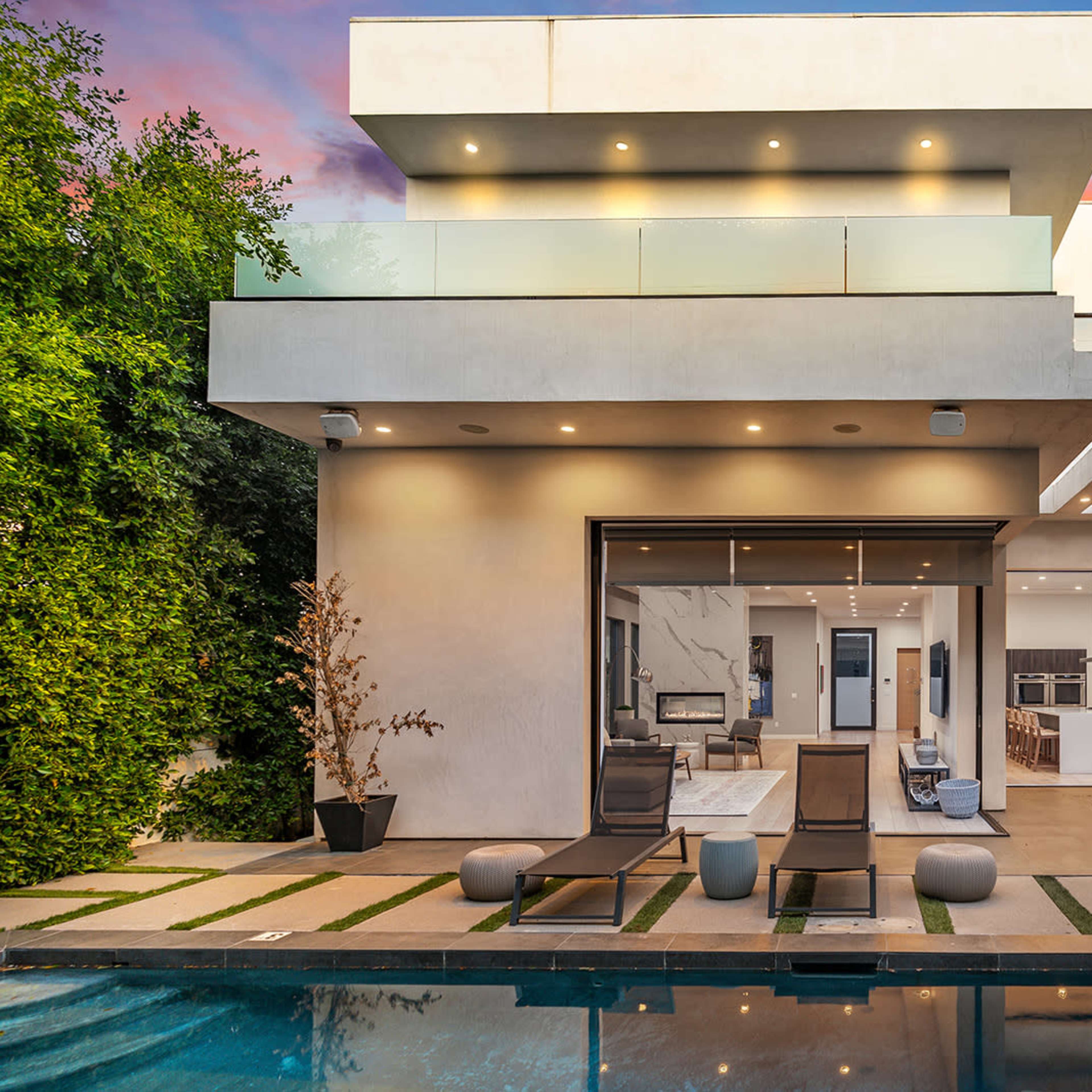 A modern two-story house features a swimming pool, outdoor seating area, and large glass doors opening to a spacious interior.