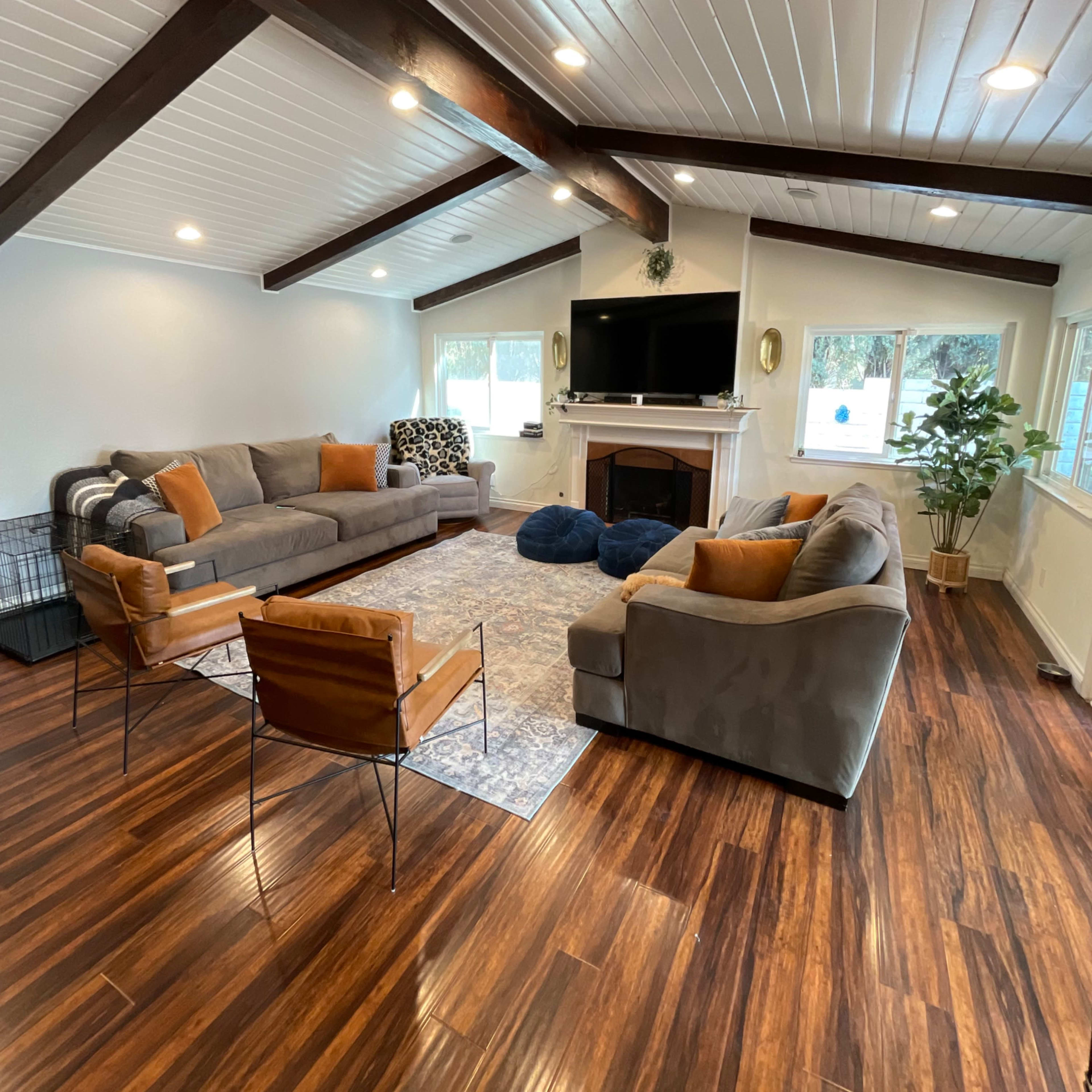A spacious living room with a hardwood floor, featuring two sofas, a coffee table, a large rug, and a television above a fireplace.